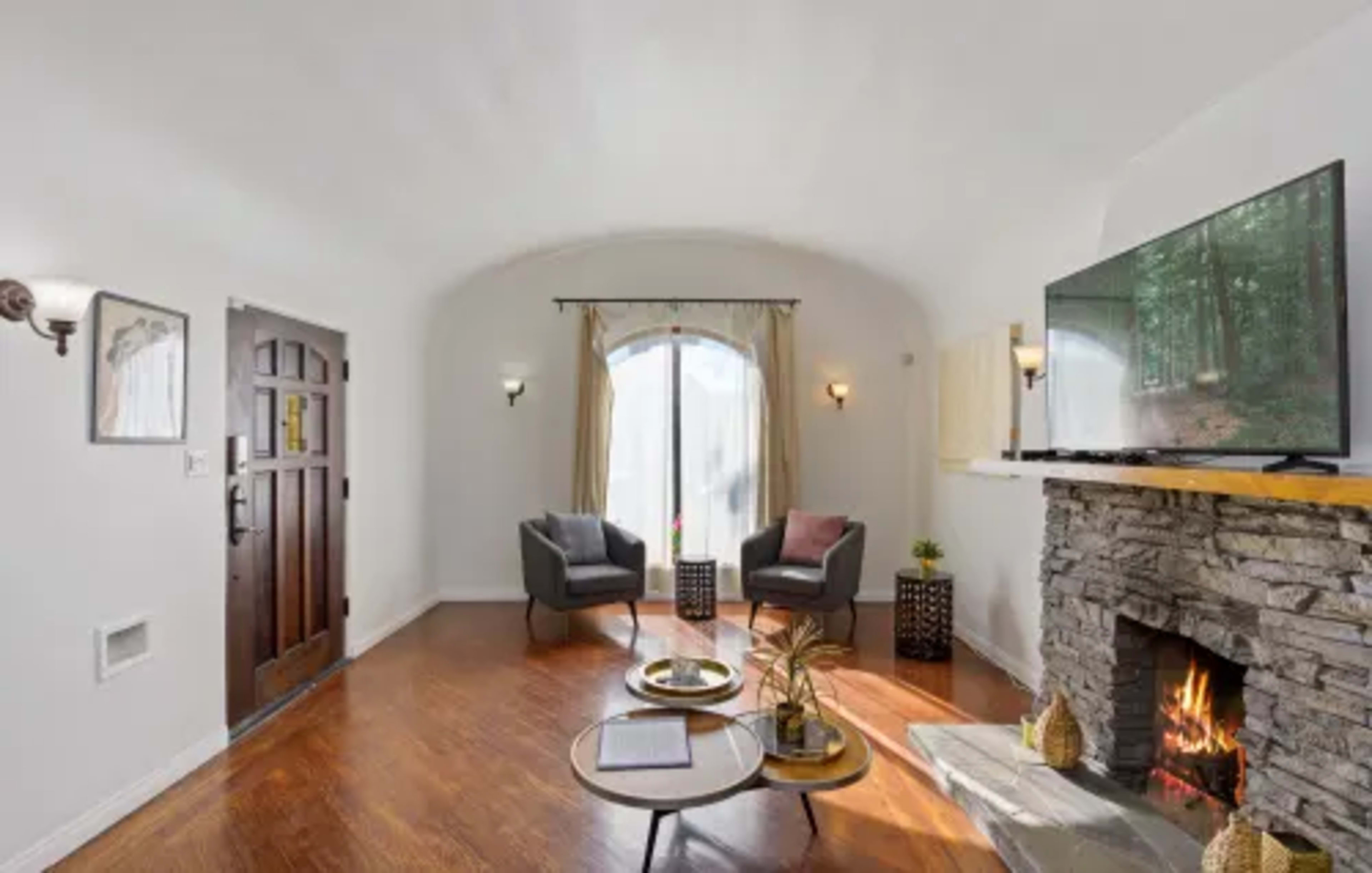 A cozy living room features two armchairs, a stone fireplace with a television mounted above, and a round coffee table with a decorative plant.