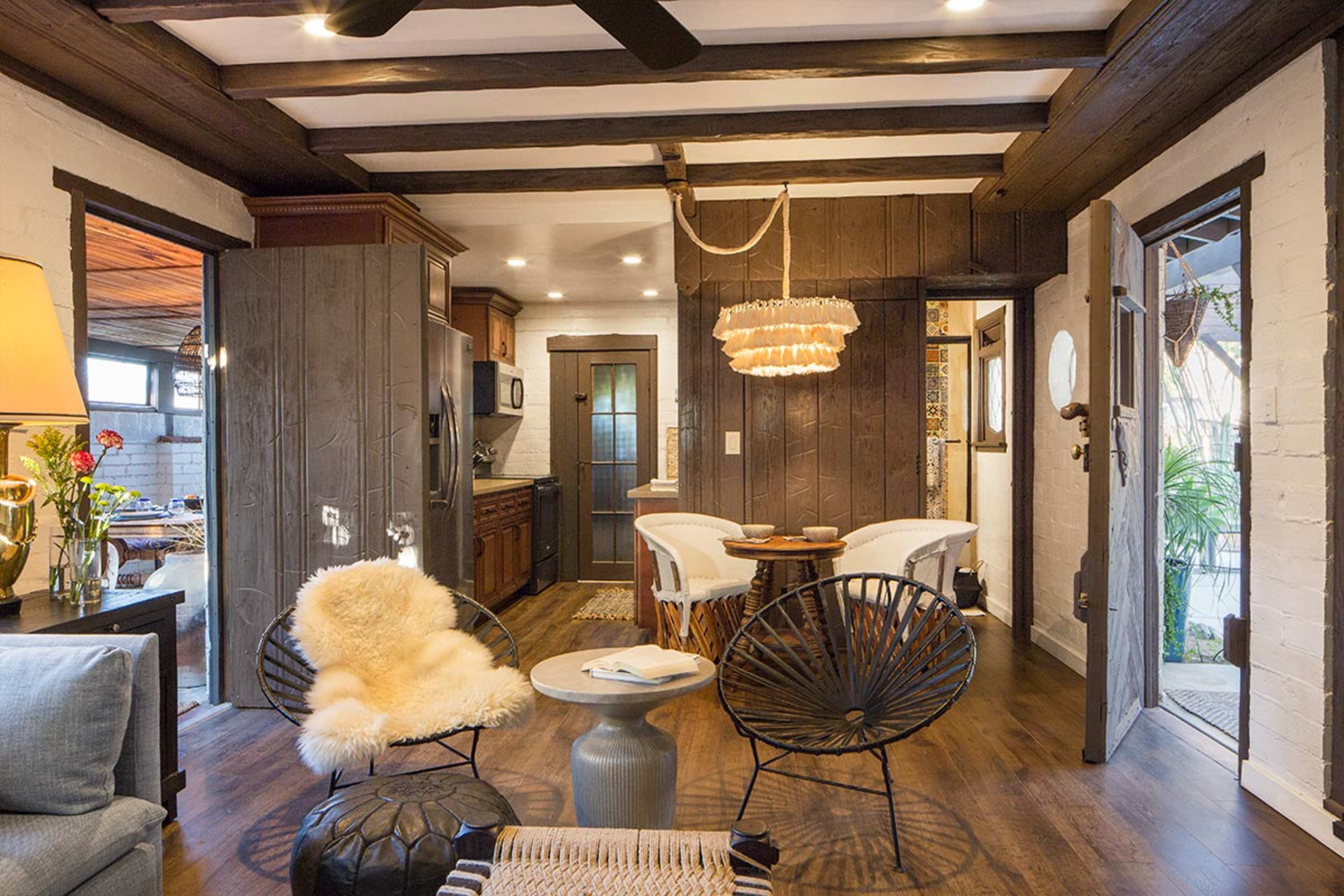 The image shows a cozy interior space featuring a living area with modern furniture, a kitchenette, and wooden beams.