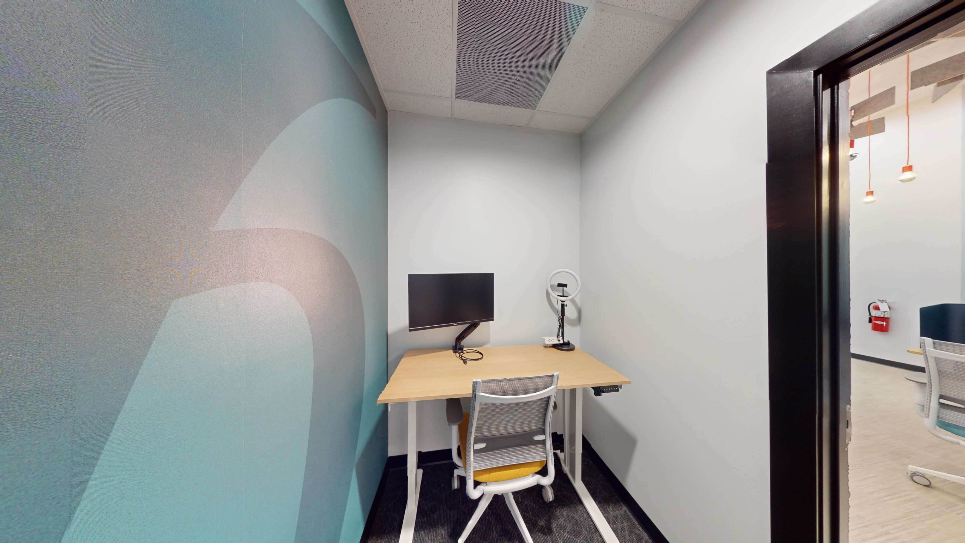 The image shows a small office space with a desk, a chair, and a computer monitor against a partially colored wall.
