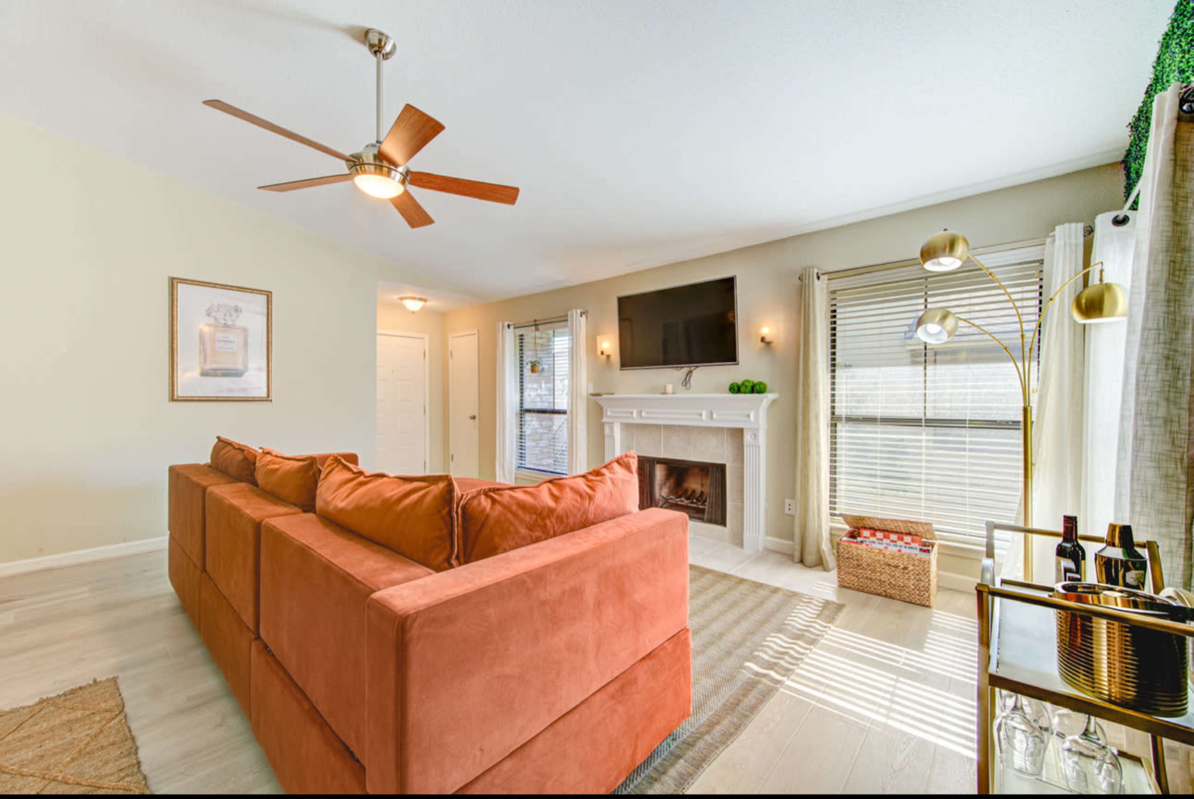 The image shows a living room with a sectional sofa, a ceiling fan, a fireplace, and a television mounted on the wall.