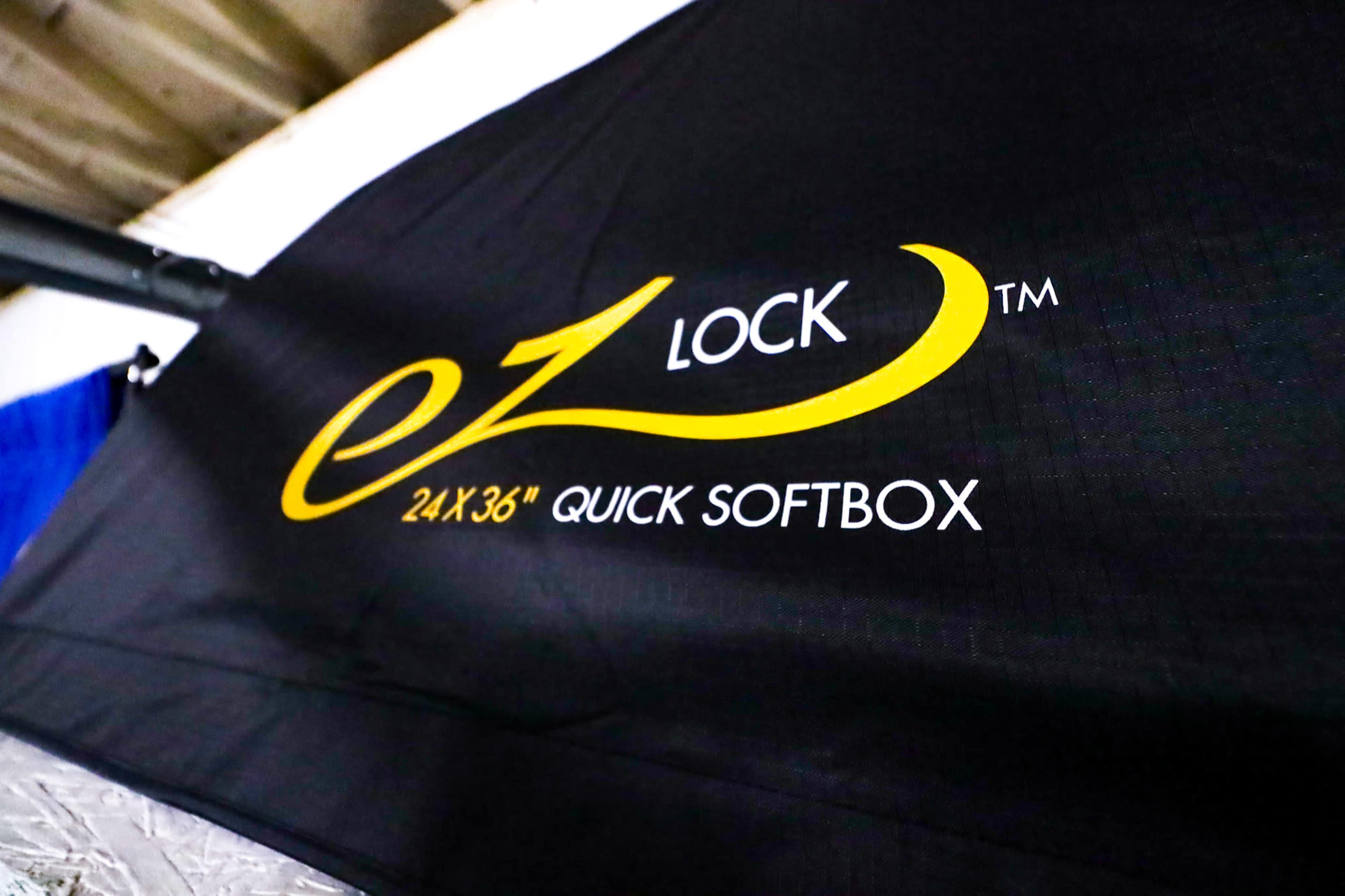 A close-up of a black fabric with a logo that reads "EZ LOCK" along with "24x36 Quick Softbox" in yellow lettering.