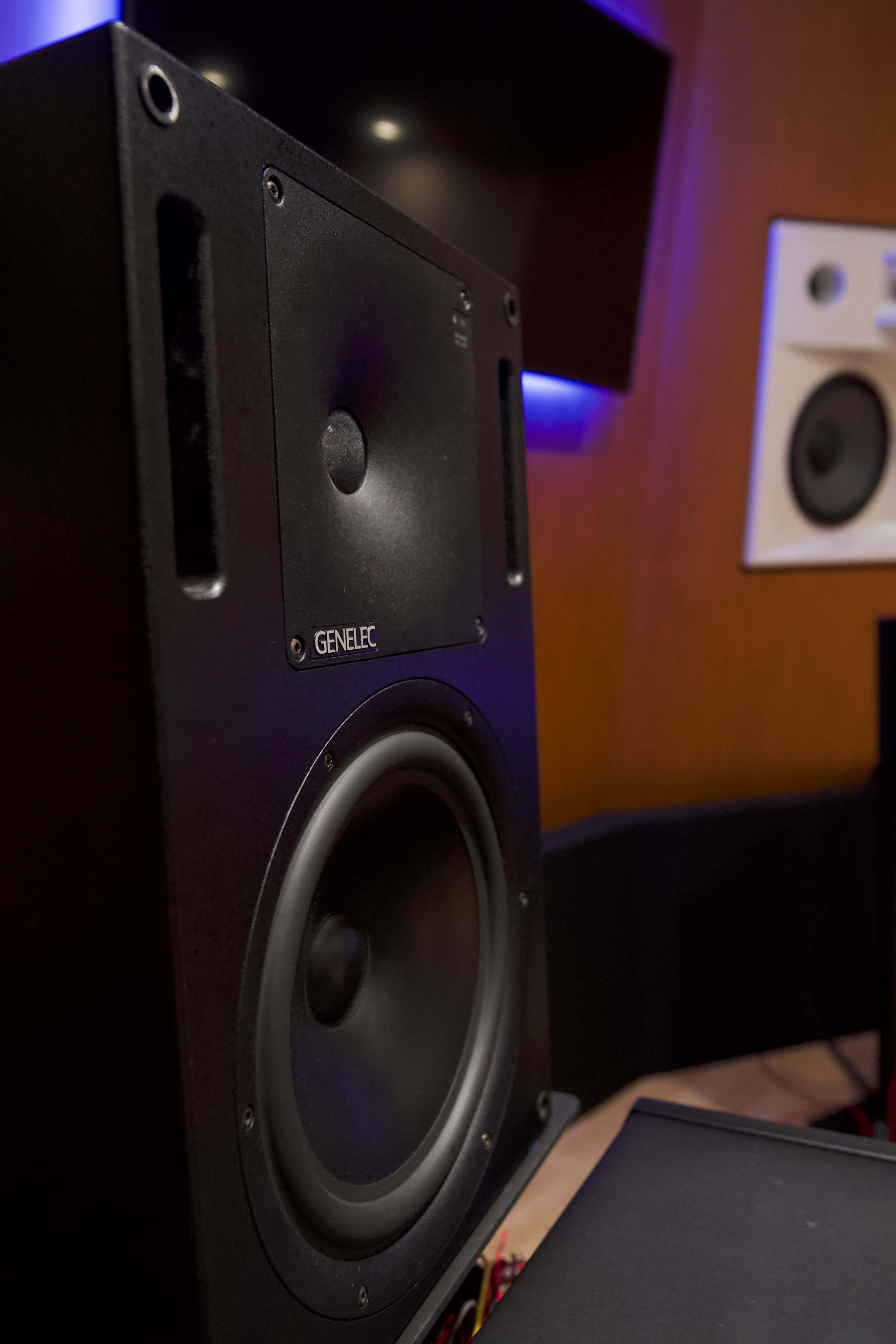 A close-up image of a Genelec speaker in a studio setting with other audio equipment in the background.