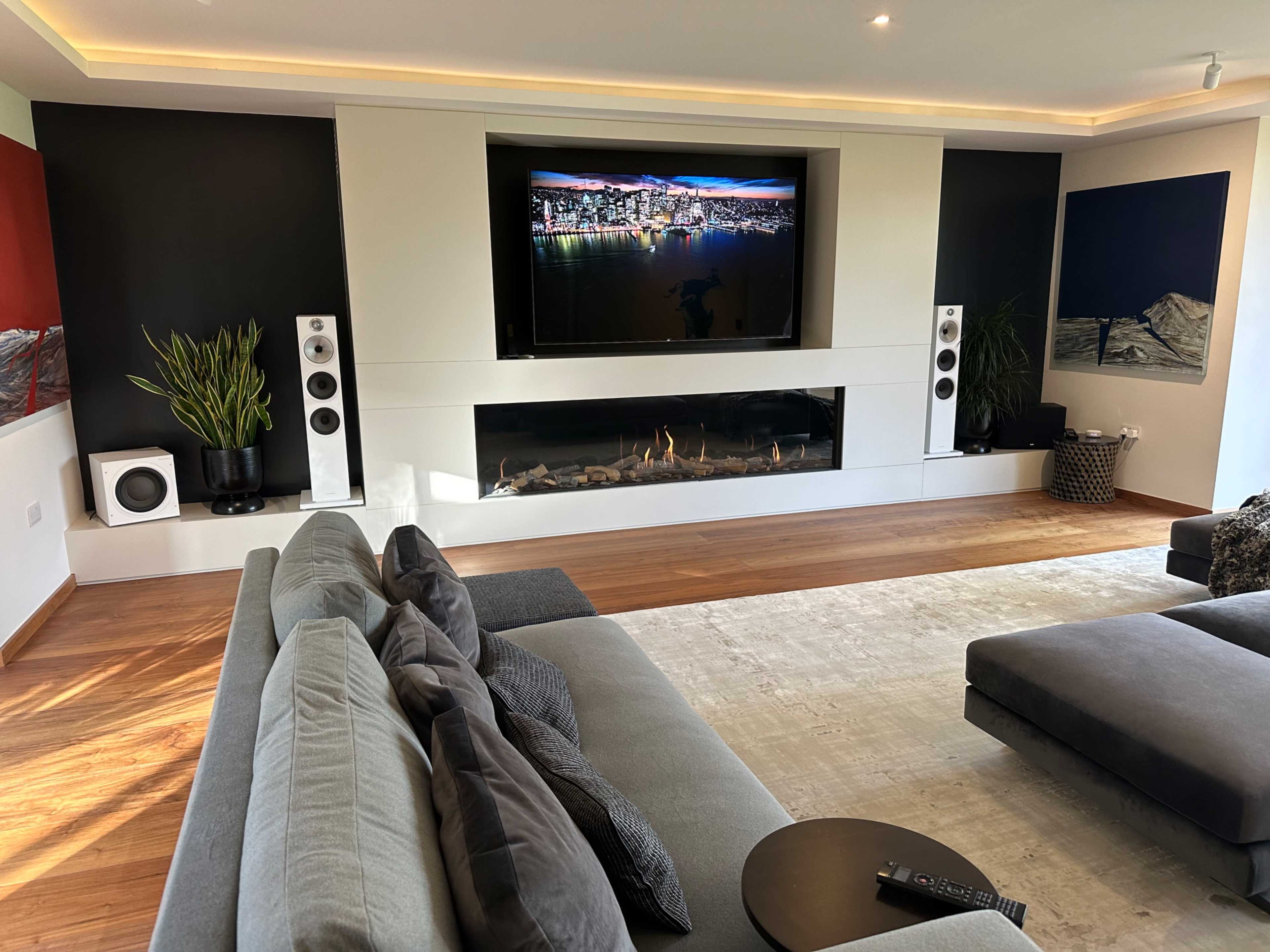 The living room features a large, wall-mounted television above a modern fireplace, with a sectional sofa and accent chairs arranged for seating.
