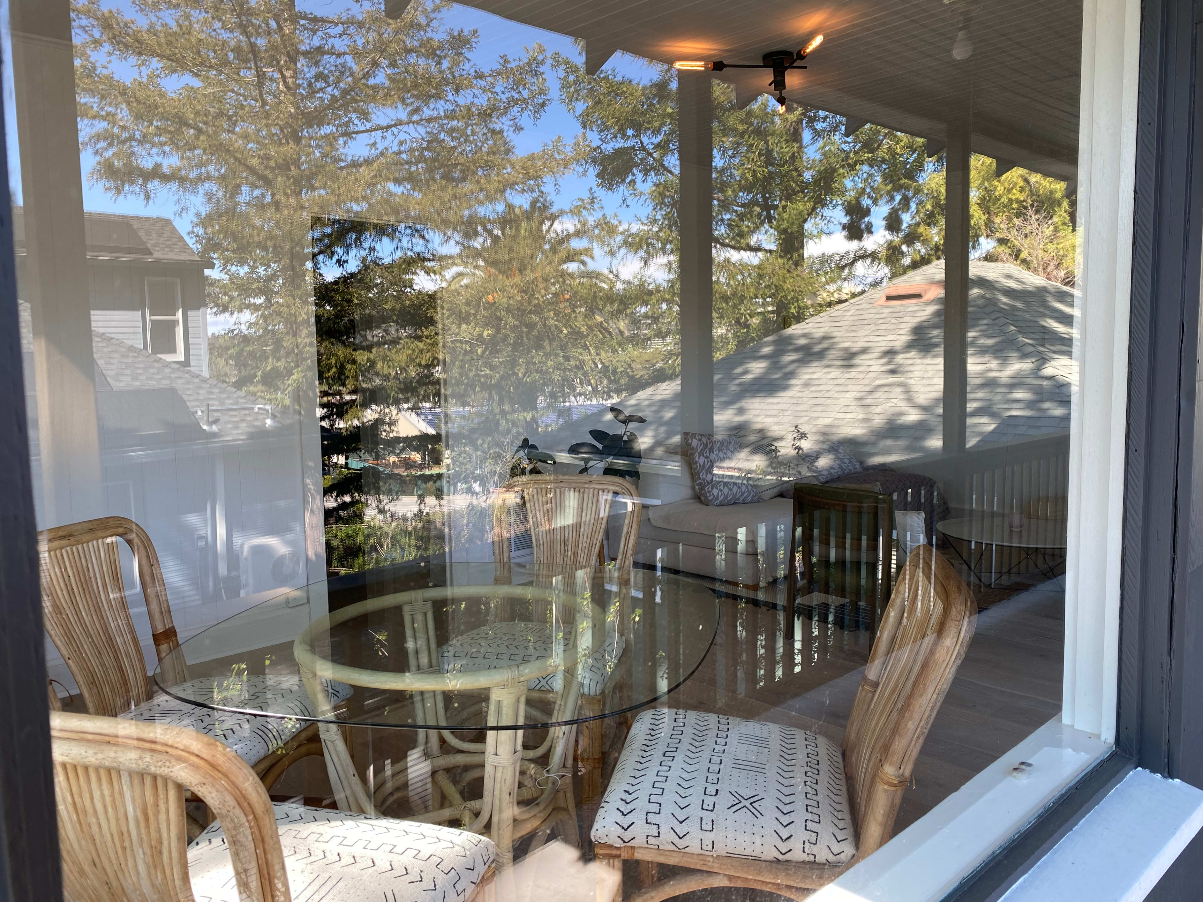 A glass-topped table with rattan chairs is visible on a porch, reflecting trees and the exterior of nearby houses.