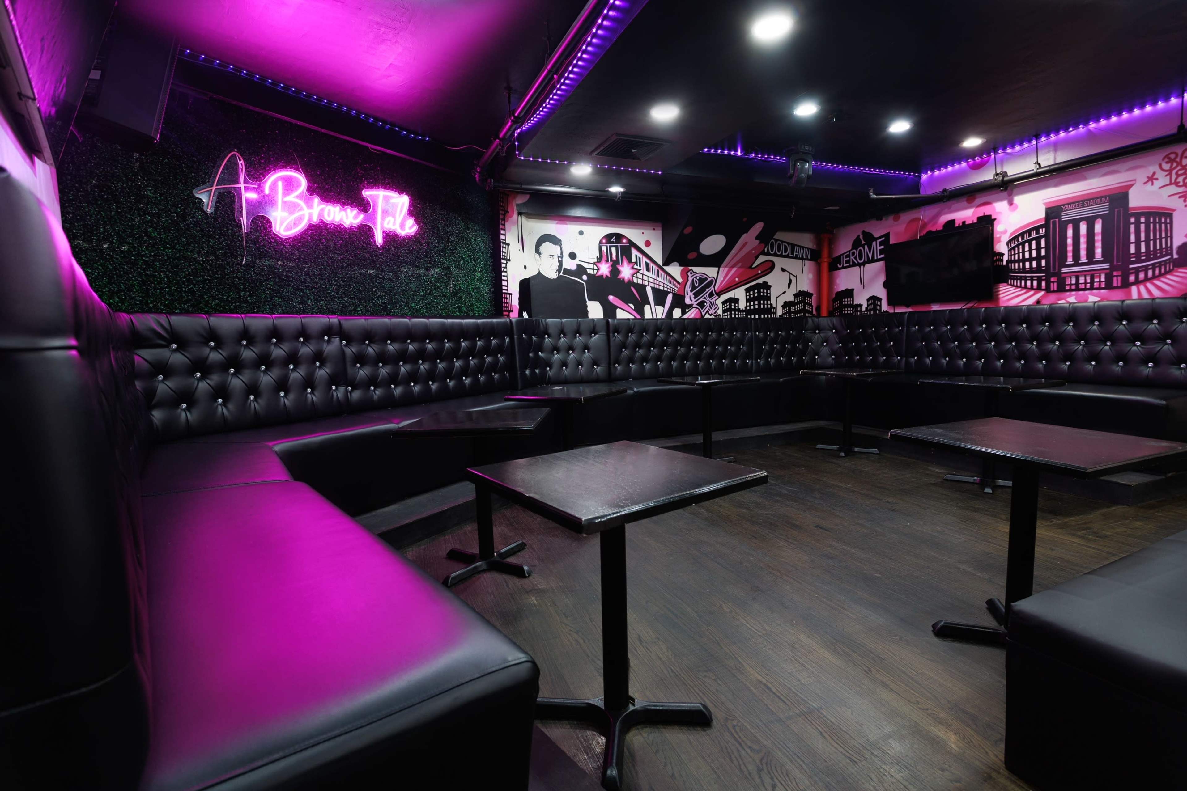 The image shows a dimly lit lounge area with black tufted seating, small tables, and vibrant pink neon lighting on the walls.