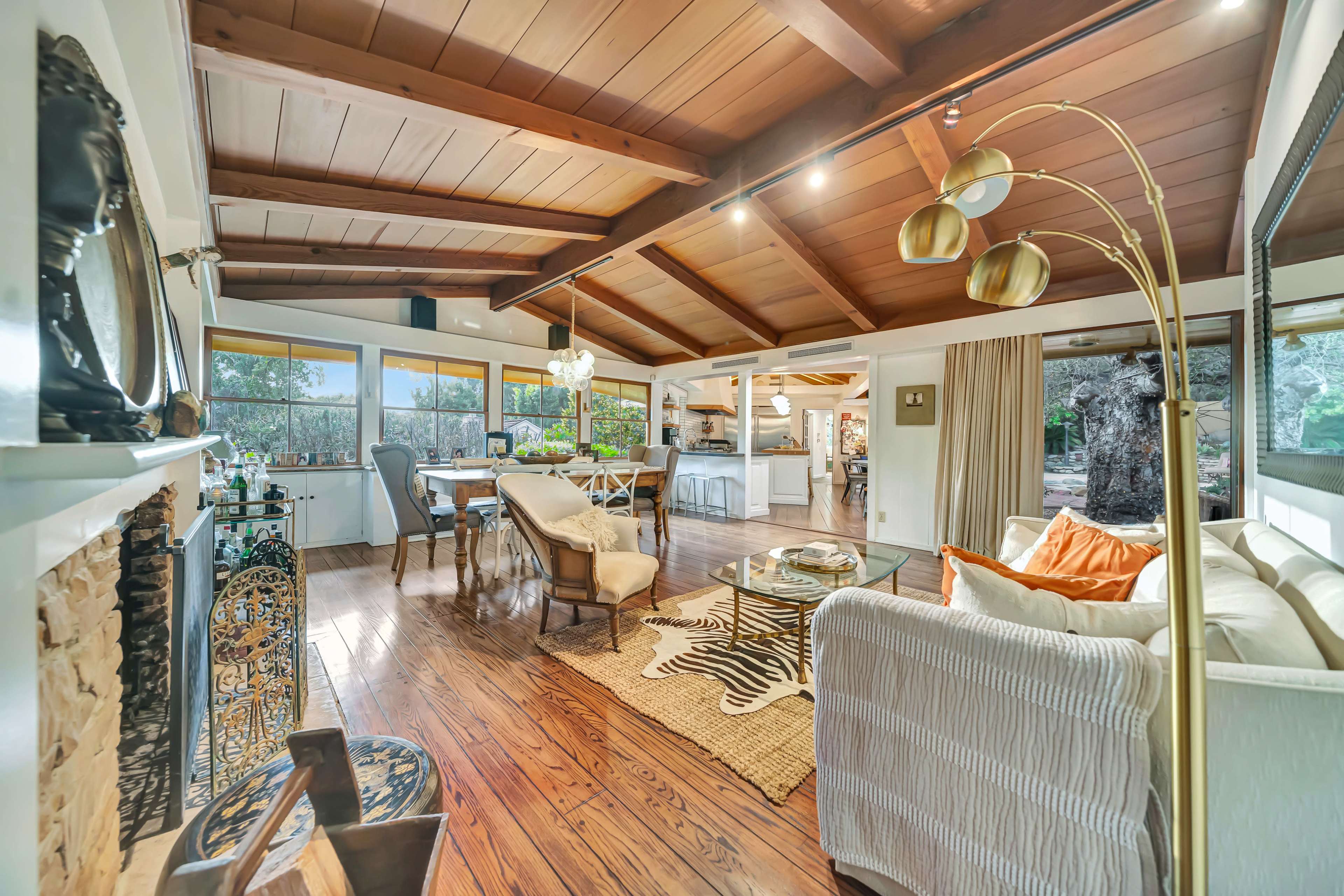 The image shows a spacious, open-concept living area with wooden beams, polished hardwood floors, and a mix of modern and traditional furniture.