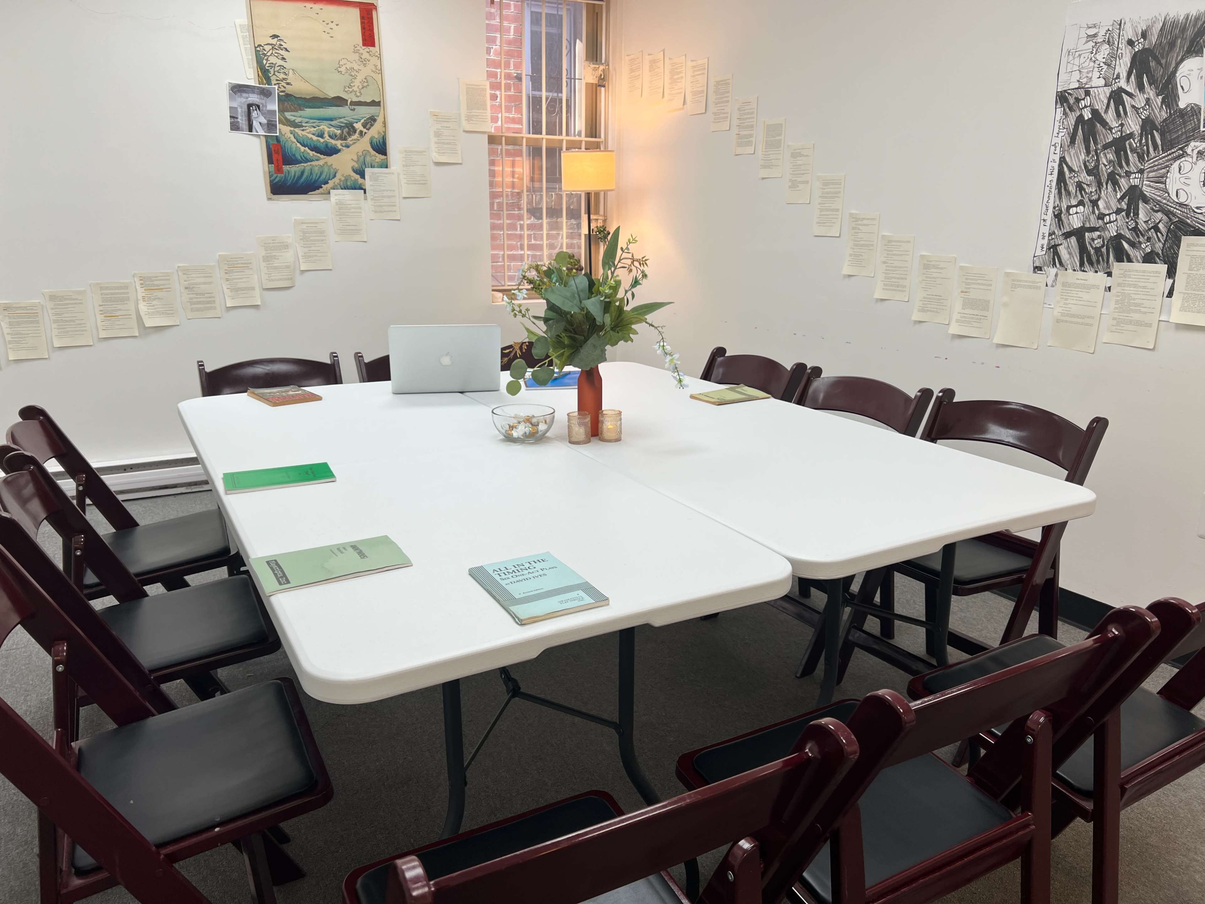 A rectangular table with chairs is set up in a room, featuring decorative papers on the walls and a laptop placed on the table.
