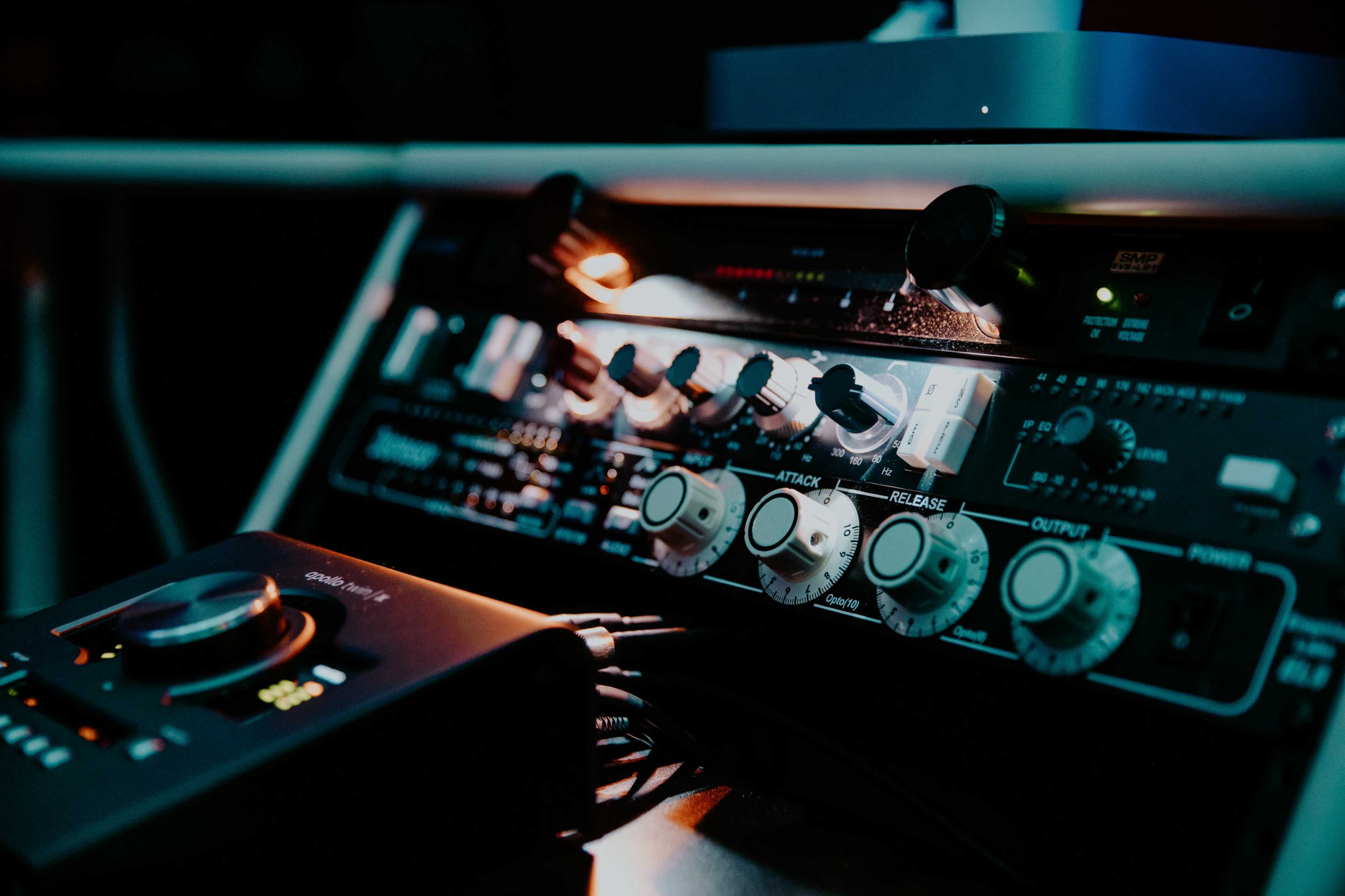 A close-up of audio equipment featuring a mixer with various knobs and a digital interface in a dimly lit environment.