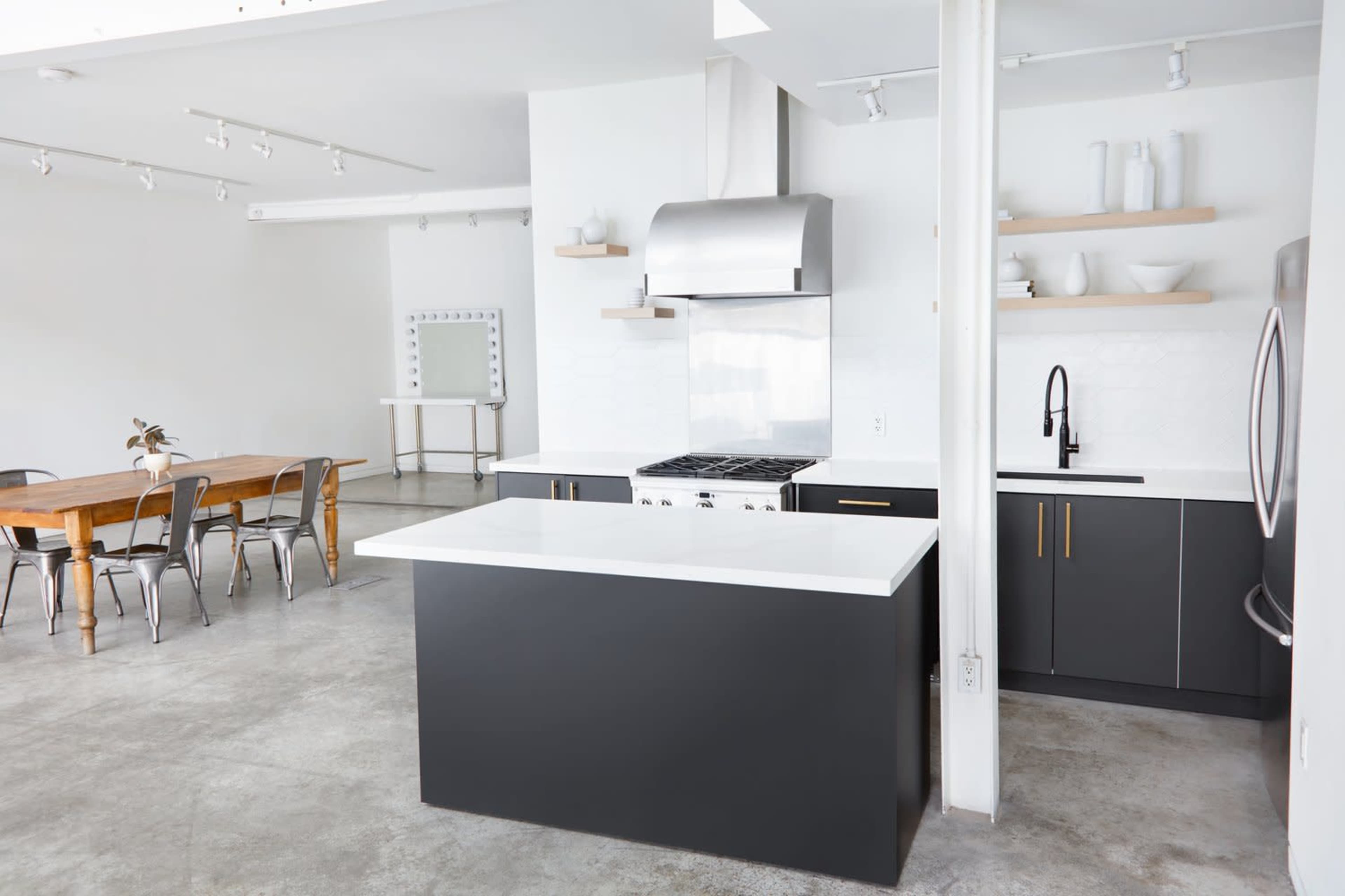 A modern kitchen with a central island, stainless steel appliances, and a dining area with a wooden table and metal chairs.