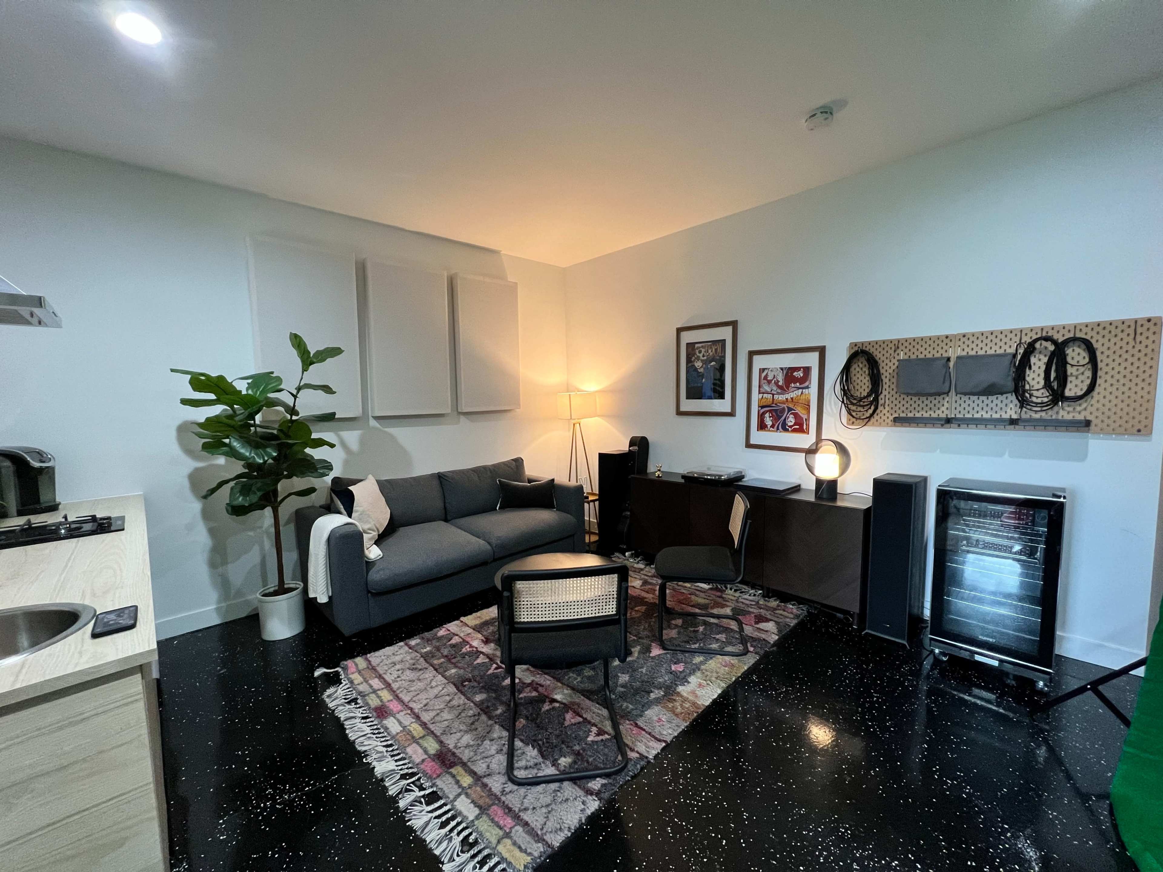 A modern living space featuring a sofa, a small workspace, a potted plant, and a mini-fridge, with patterned flooring and a decorative rug.