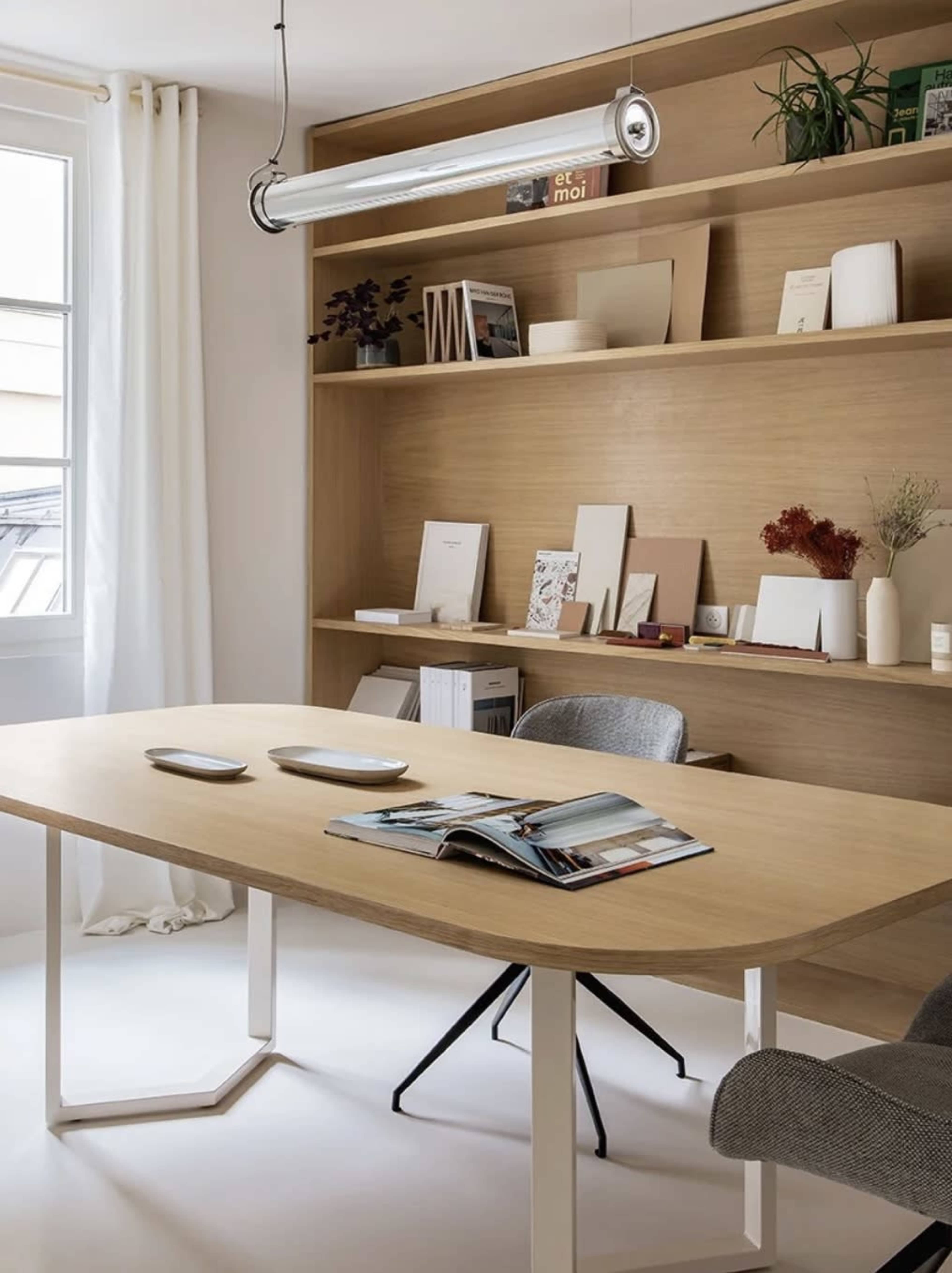 A minimalist workspace features a wooden table with two plates, an open magazine, and a neatly organized shelf displaying various items.