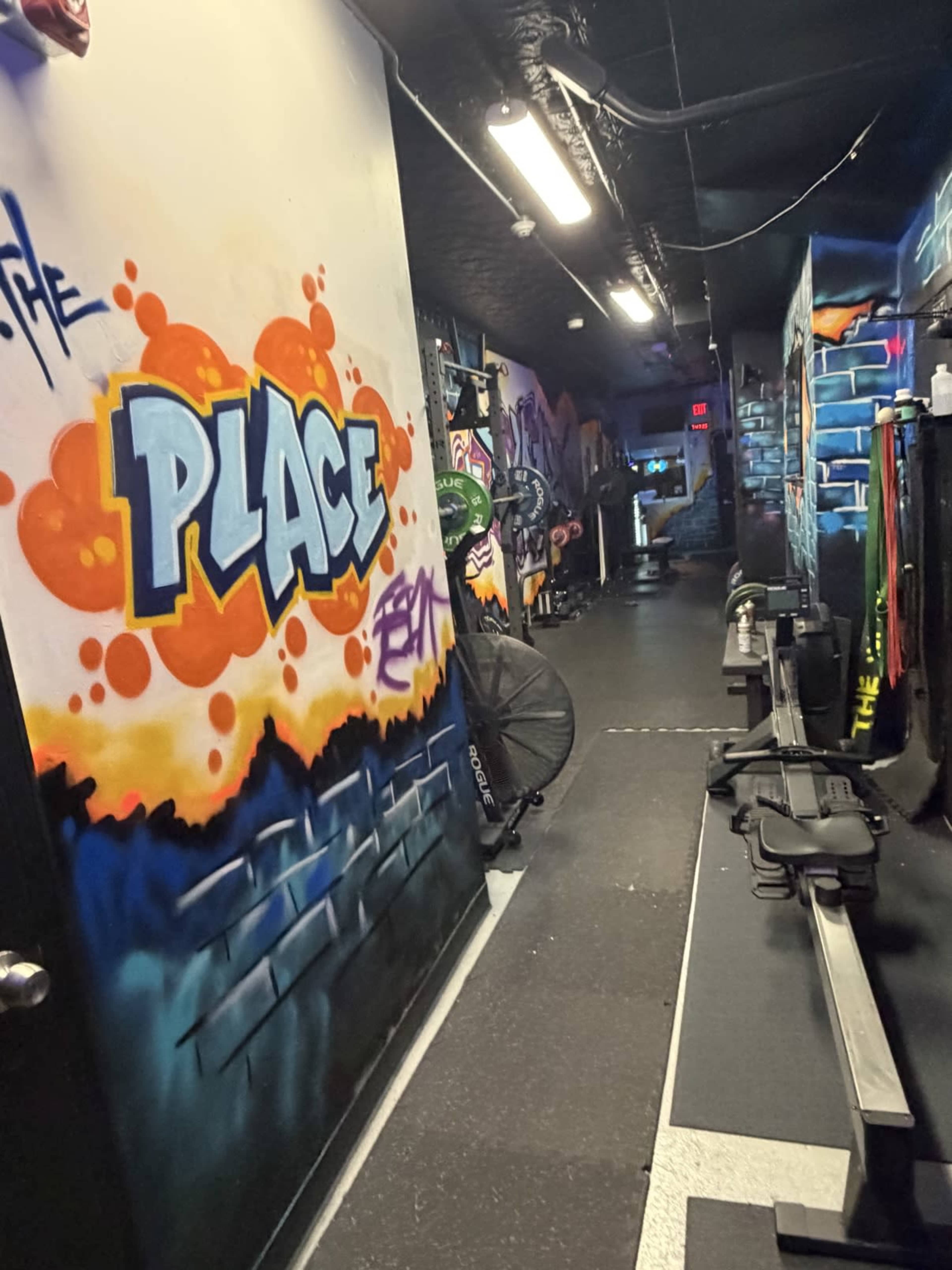 The image shows a narrow hallway adorned with vibrant graffiti art, leading to a fitness area with exercise equipment visible along the sides.