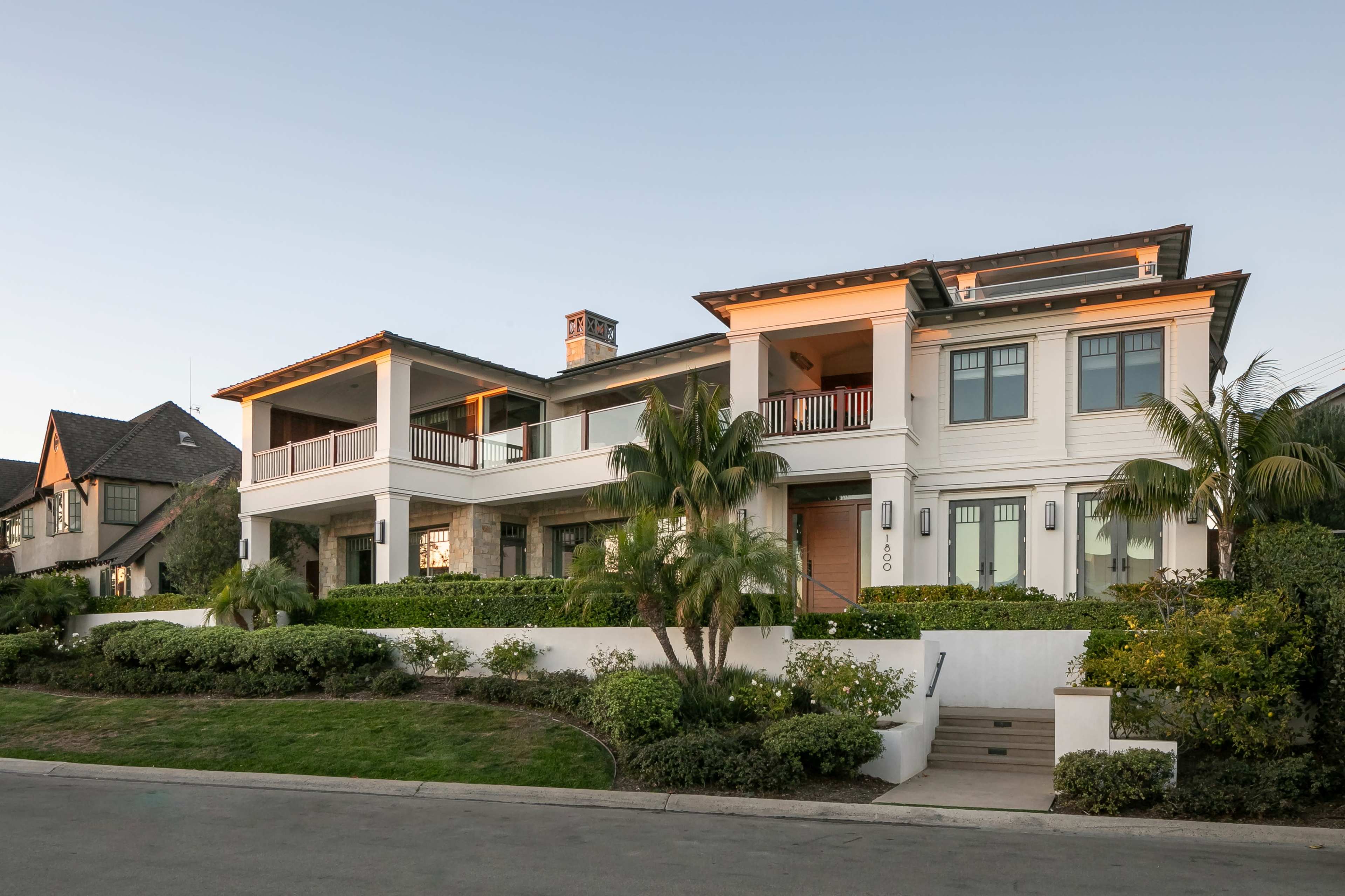 A large, two-story modern house with a stone facade and landscaped gardens is situated on a quiet street.