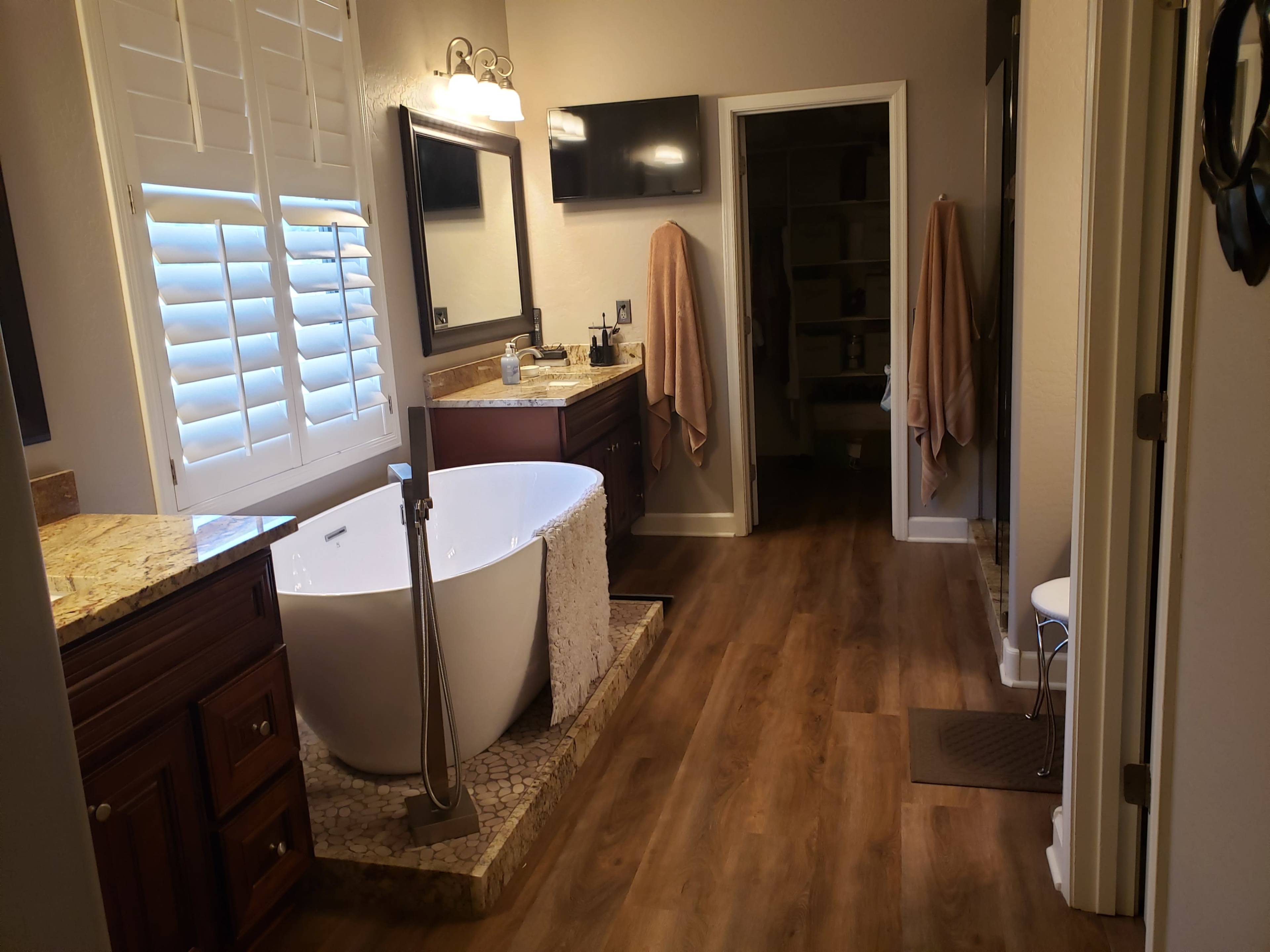 A modern bathroom features a freestanding tub, dual sinks with wooden cabinetry, and a well-lit space with a door leading to a closet.