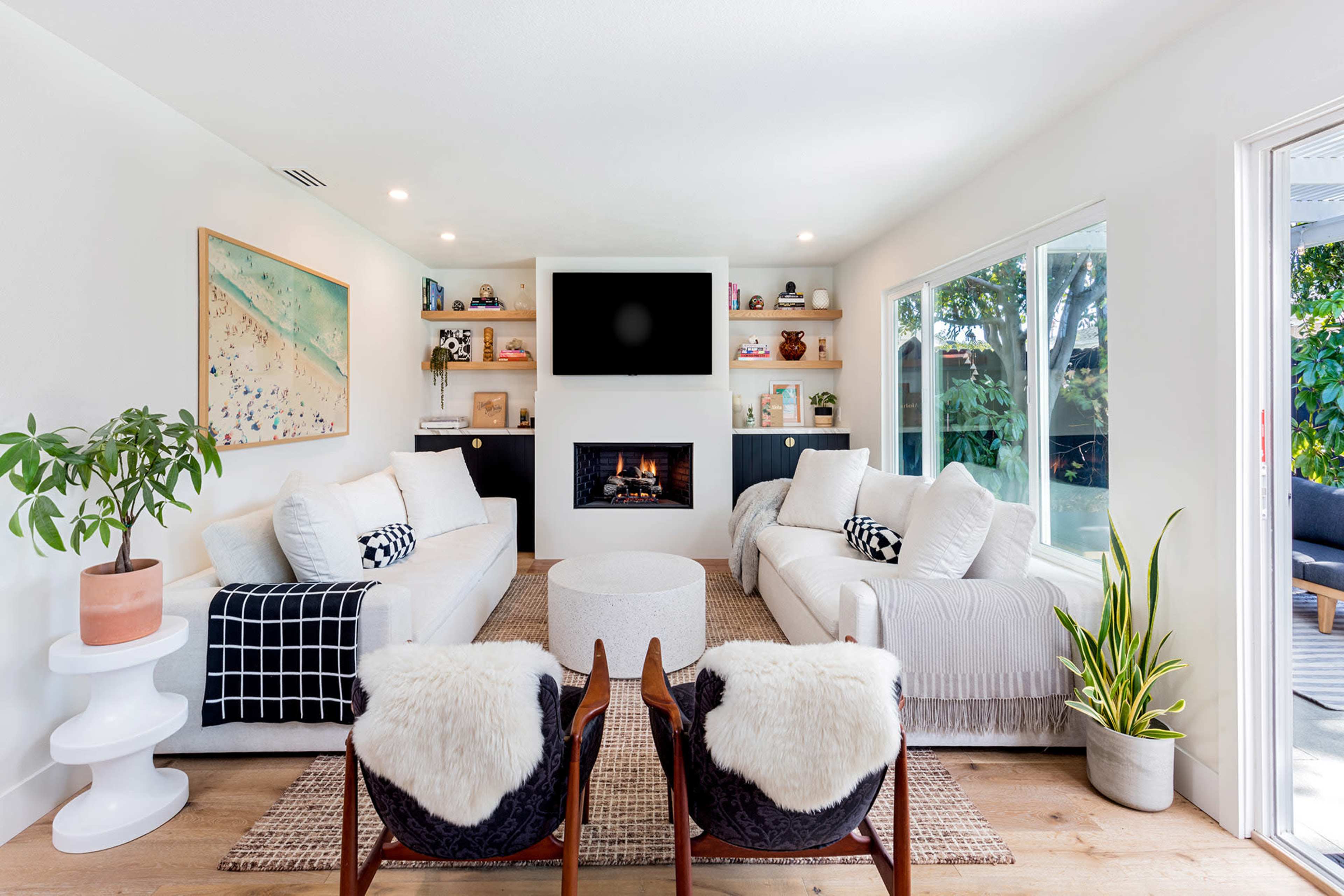 A modern living room featuring two sectional sofas, a fireplace with a TV mounted above it, and a round coffee table, all arranged around a woven area rug.