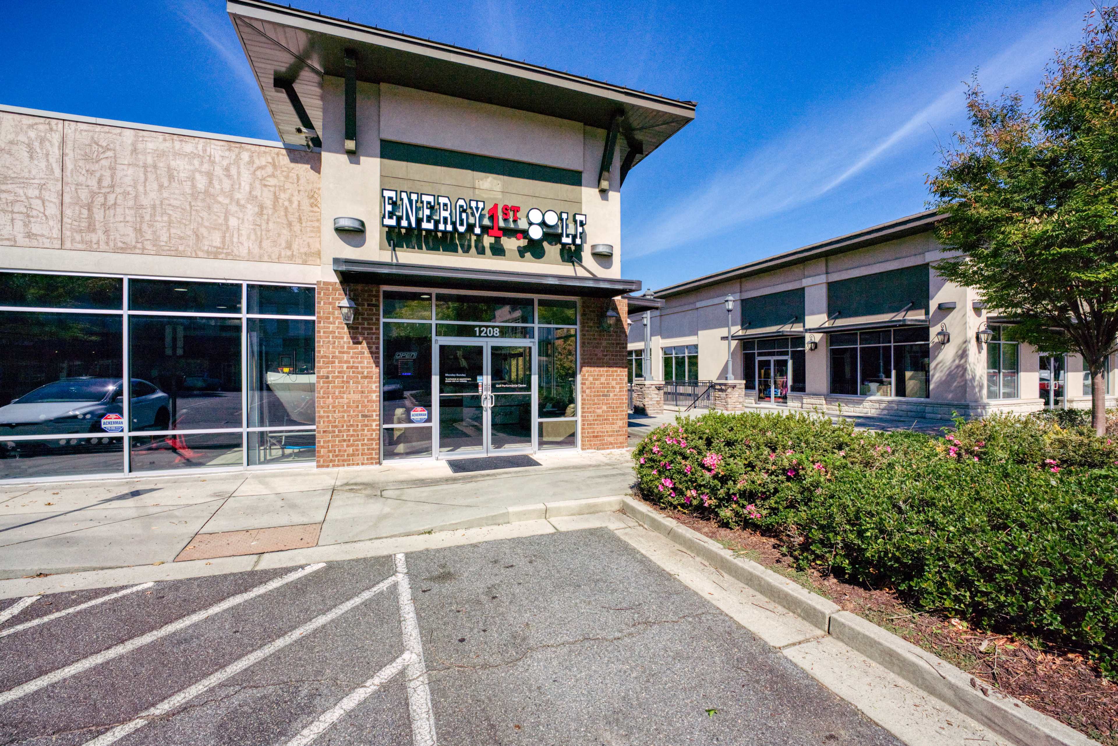 A commercial building with a storefront labeled "Energy 1st Golf" and a parking area in front, surrounded by landscaping.