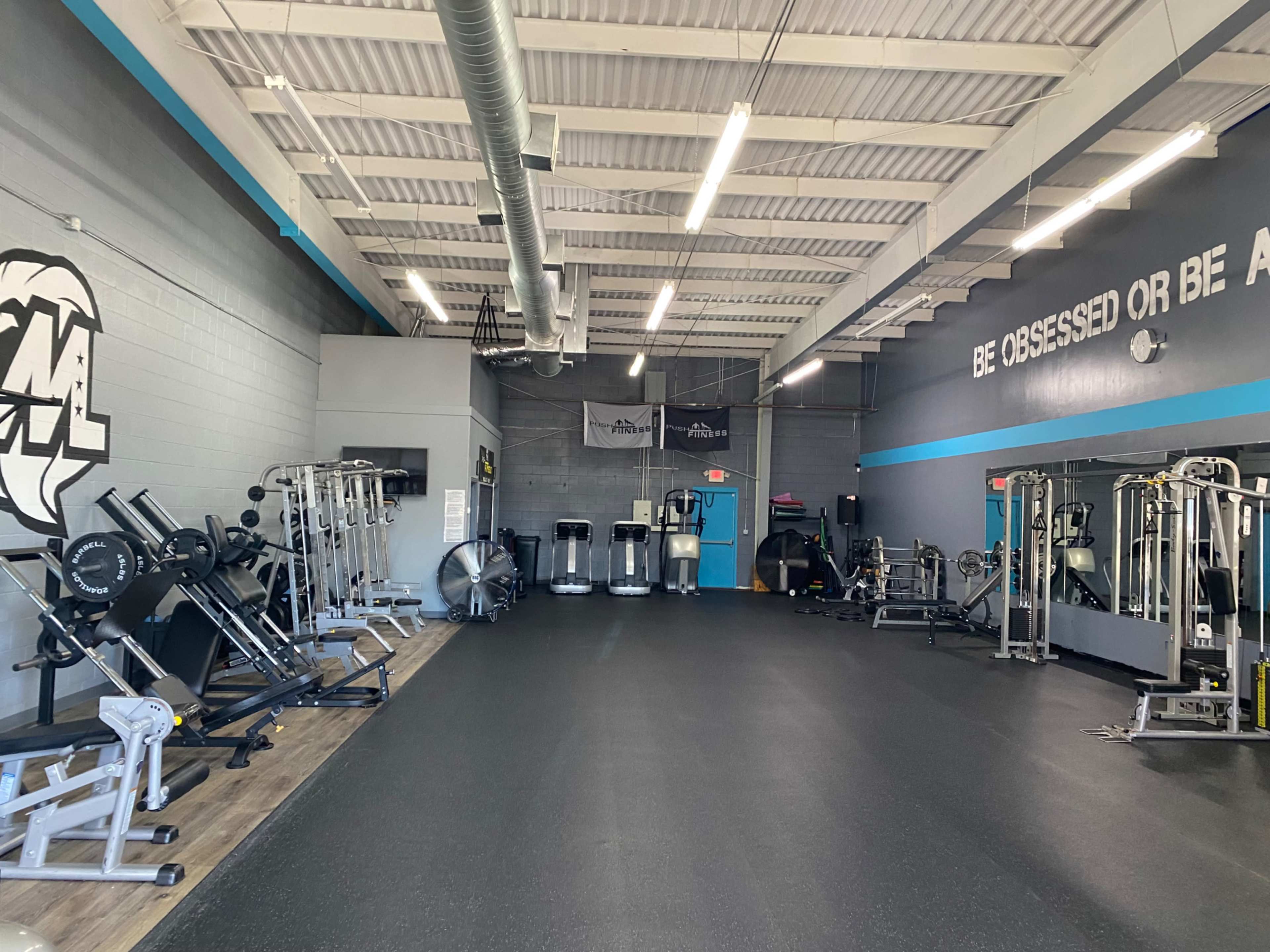 The image shows a spacious gym equipped with various weightlifting machines, cardio equipment, and a large mirrored wall.