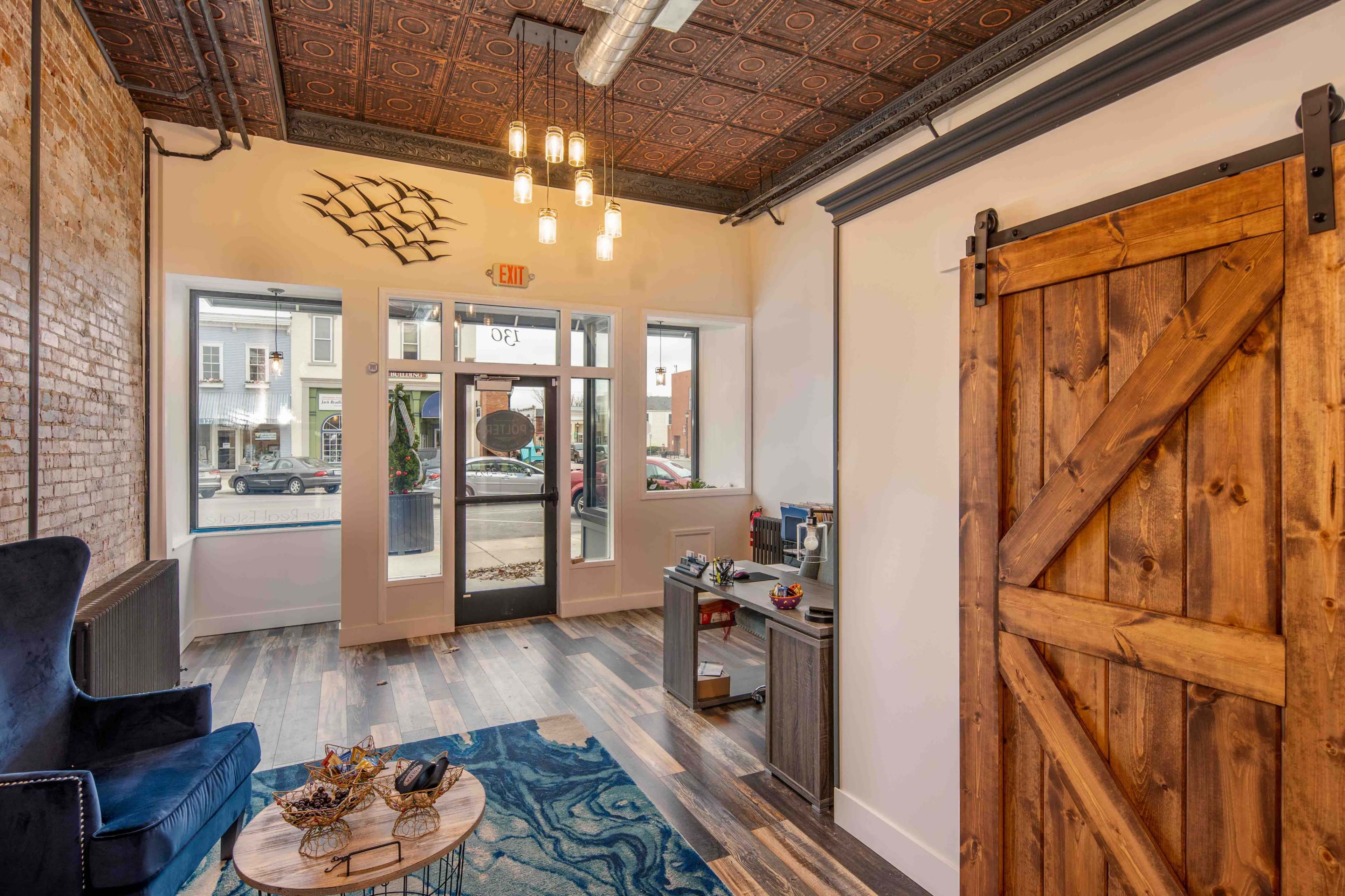A well-lit interior space featuring a wooden barn door, a blue rug, and modern furniture set against a brick wall with a patterned ceiling.