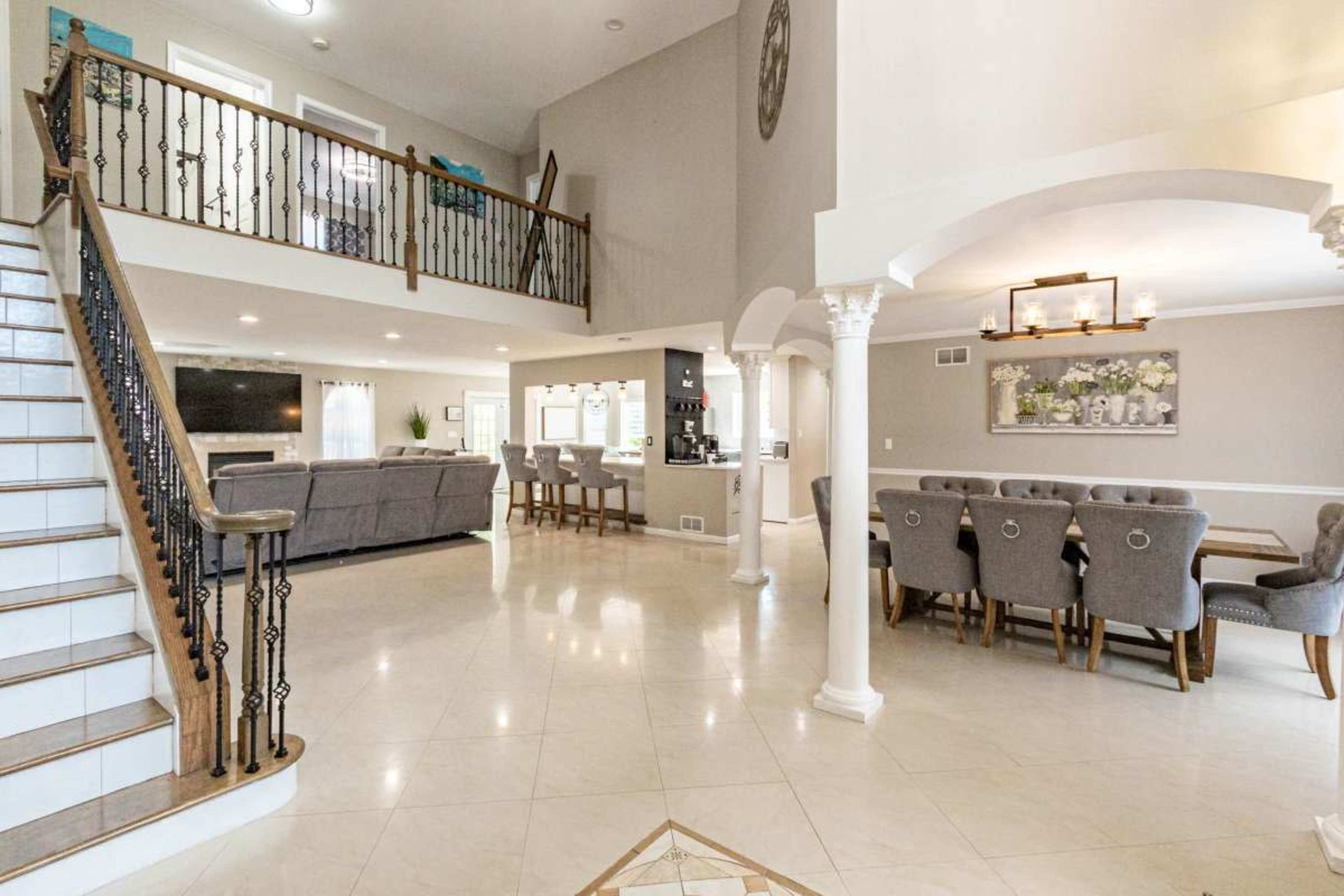 The image shows a spacious, two-story living area with a staircase, seating area, and dining space.