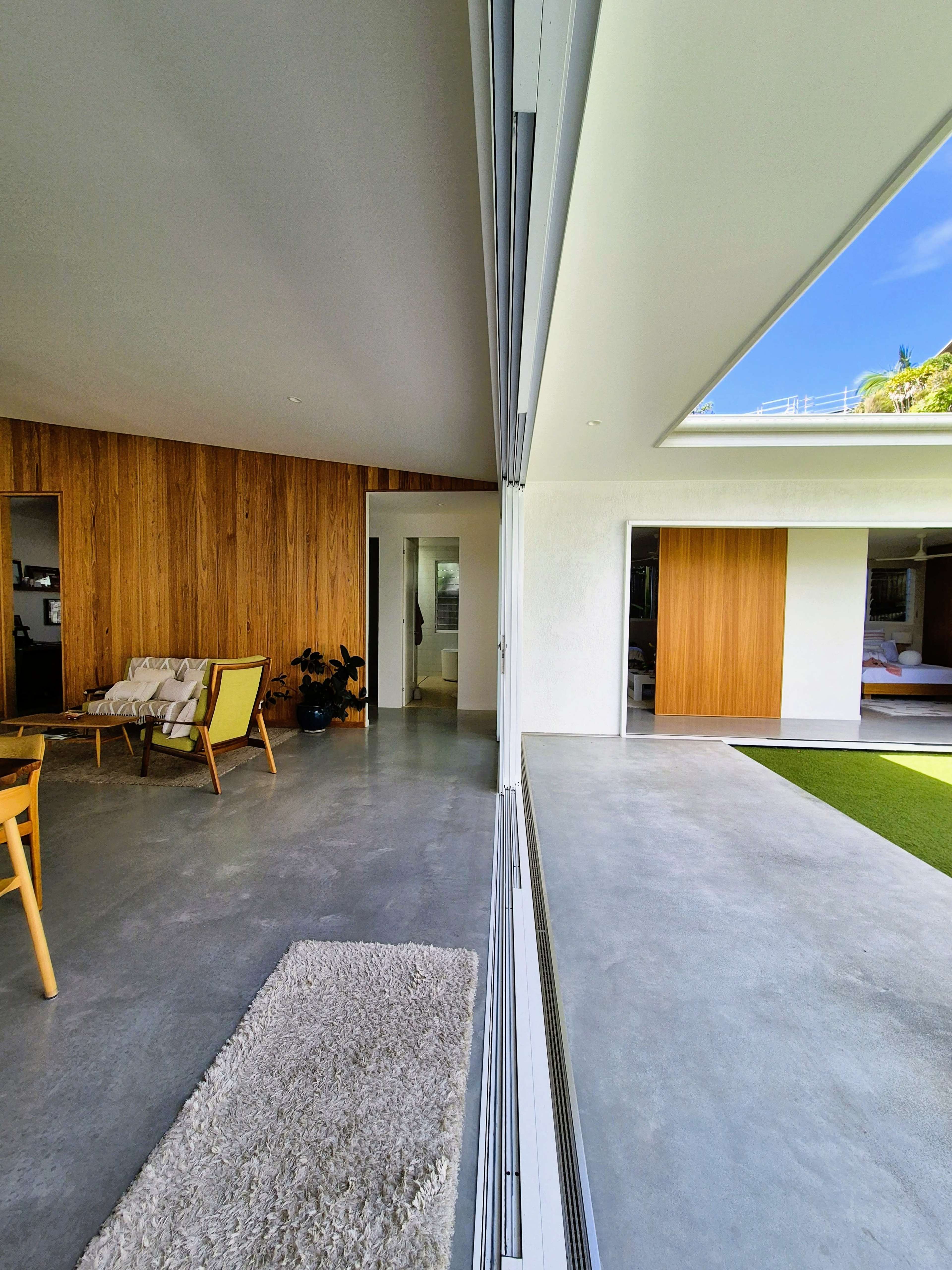 The image shows a modern interior space with a smooth concrete floor, wooden walls, and large sliding glass doors leading to an outdoor area.