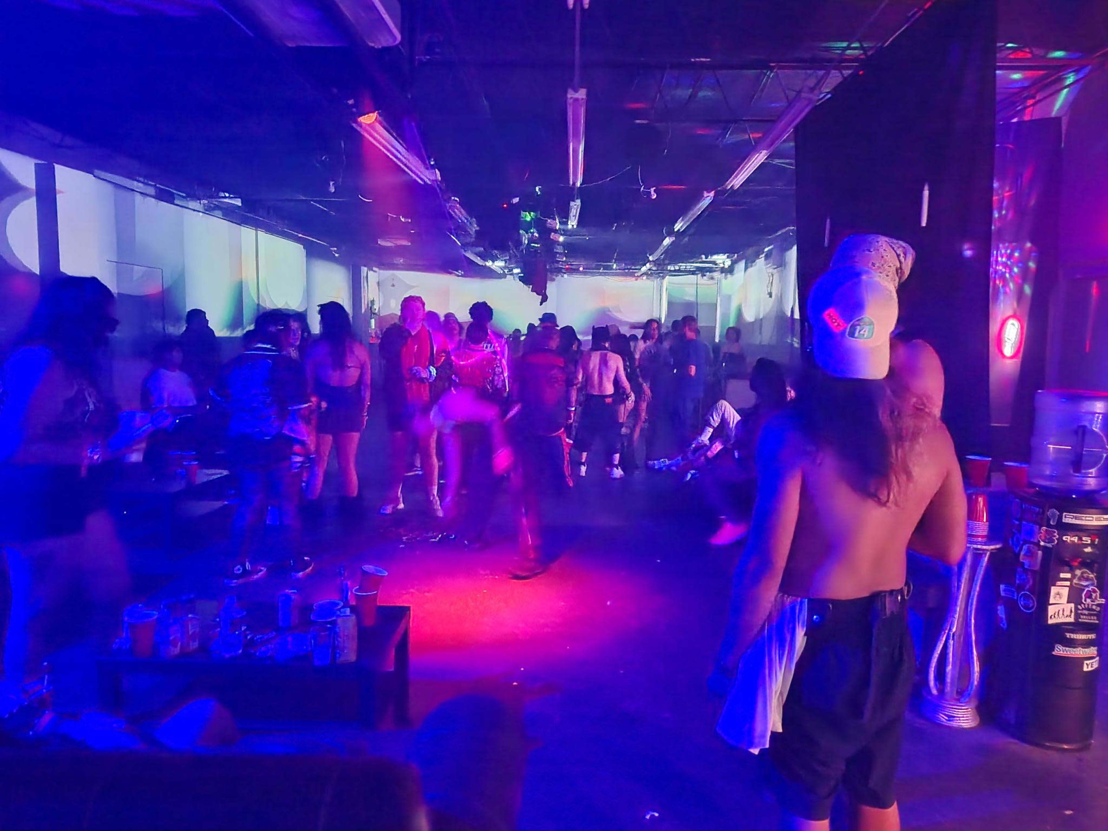 A crowded venue filled with people dancing and socializing under colorful lights.