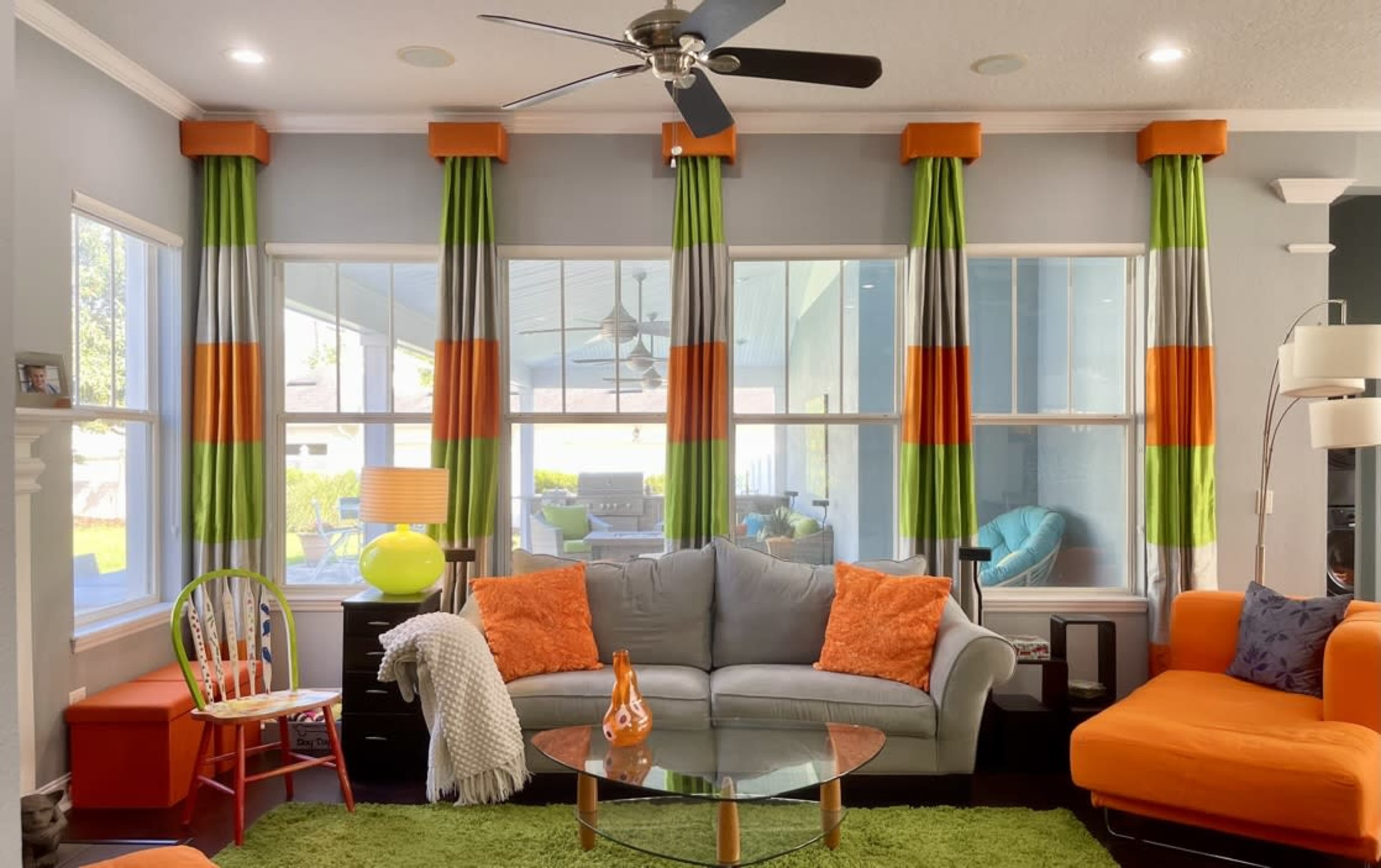 The living room features a gray sofa, an orange accent chair, and colorful curtains with green, orange, and gray stripes, highlighted by a circular glass coffee table.