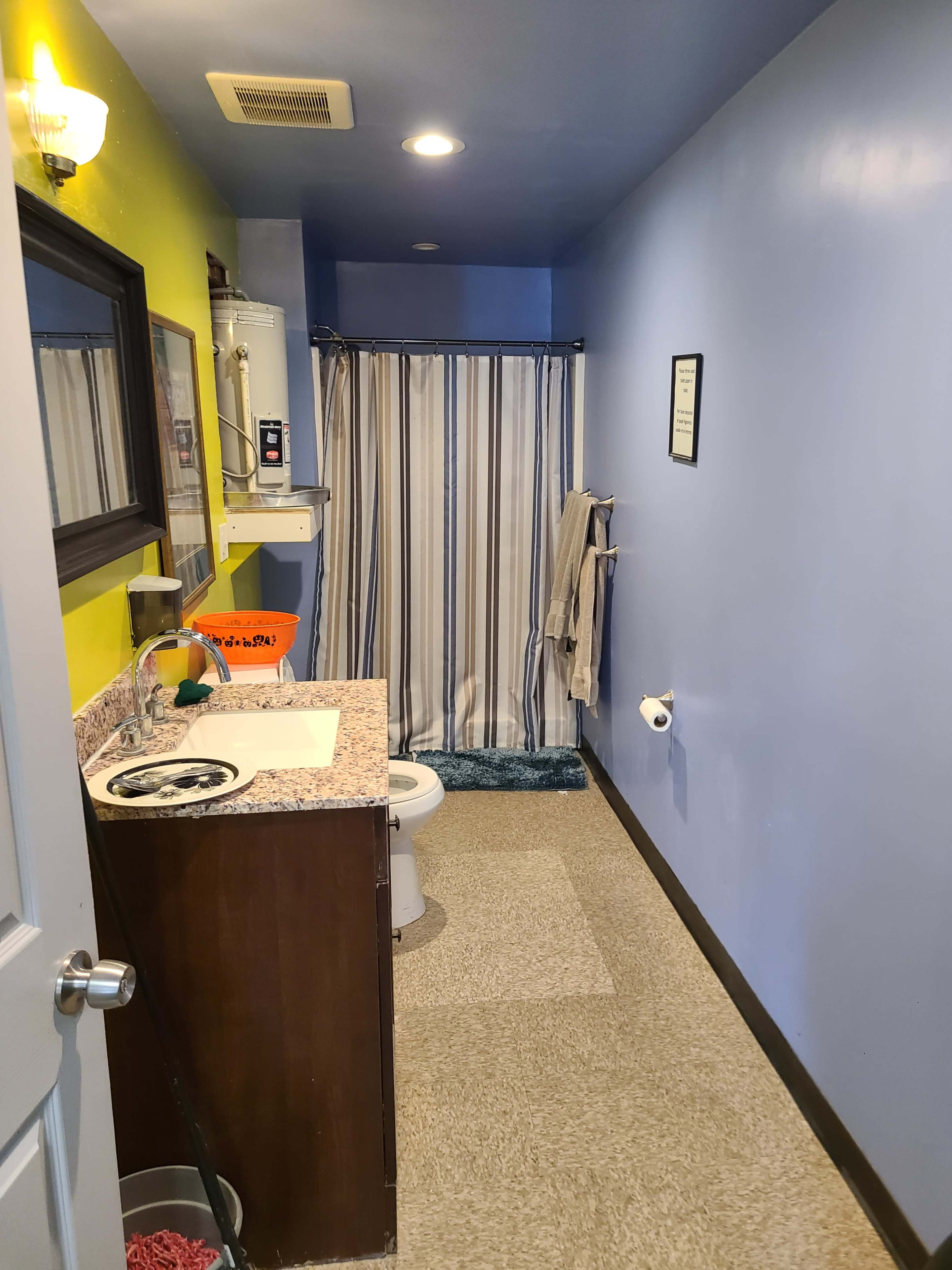 A bathroom featuring a blue and yellow color scheme, with a shower curtain, sink with a countertop, toilet, and a towel hanging on the wall.