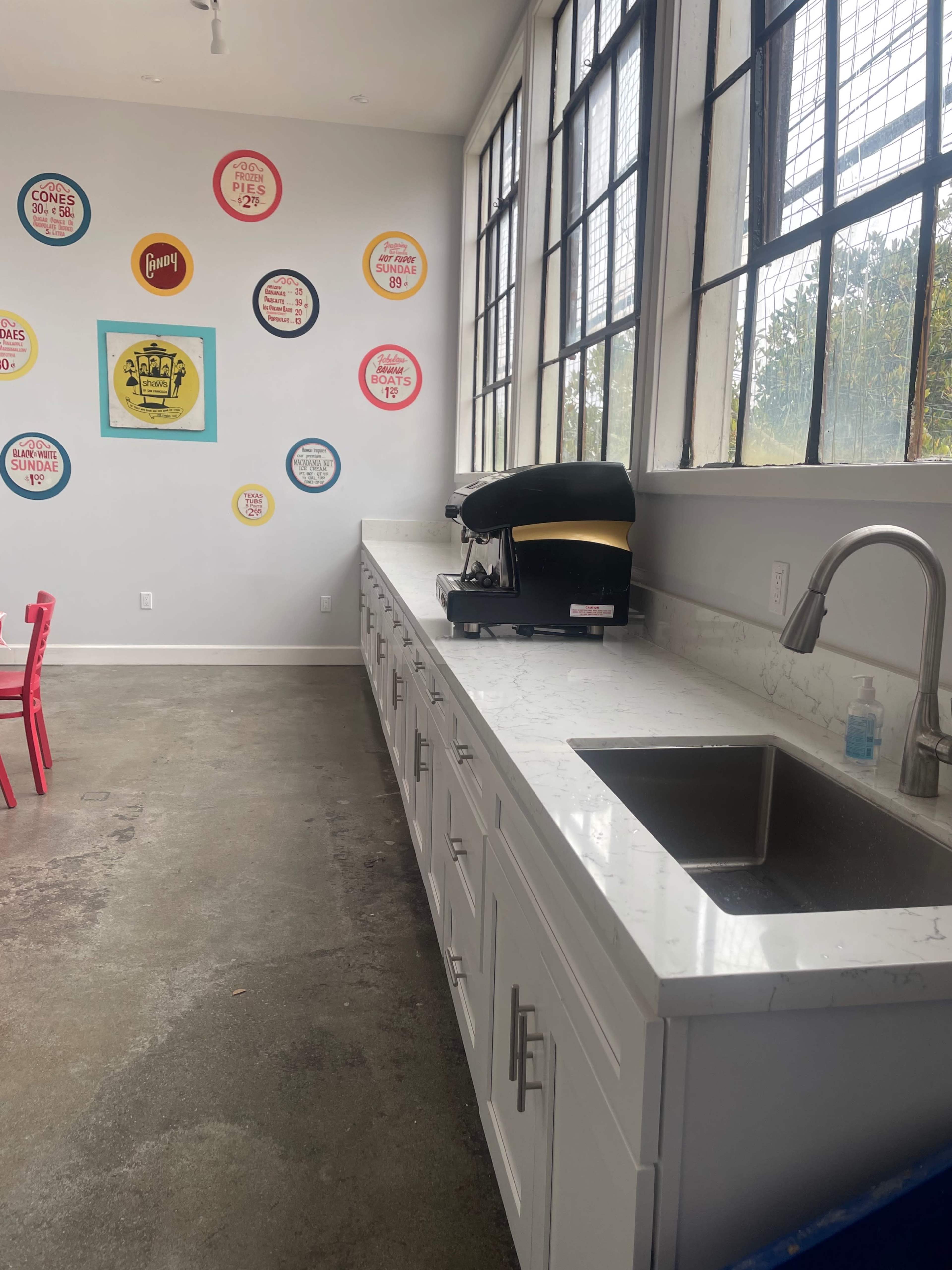 A modern kitchen with a long white countertop, a sink, and a black coffee maker against a wall decorated with colorful circular wall art.