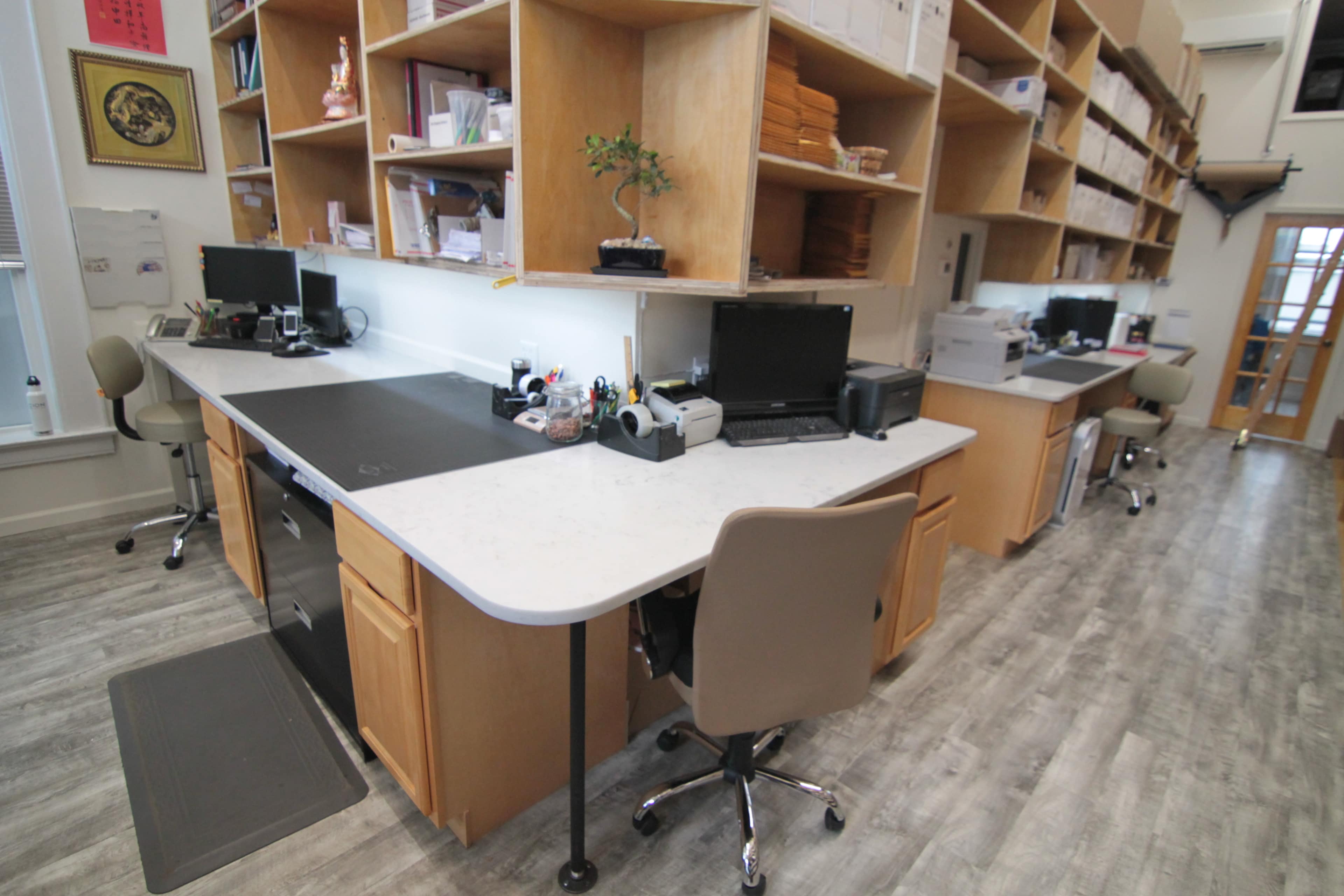 A modern office space with multiple desks equipped with computers and office supplies, surrounded by wooden shelves filled with documents.