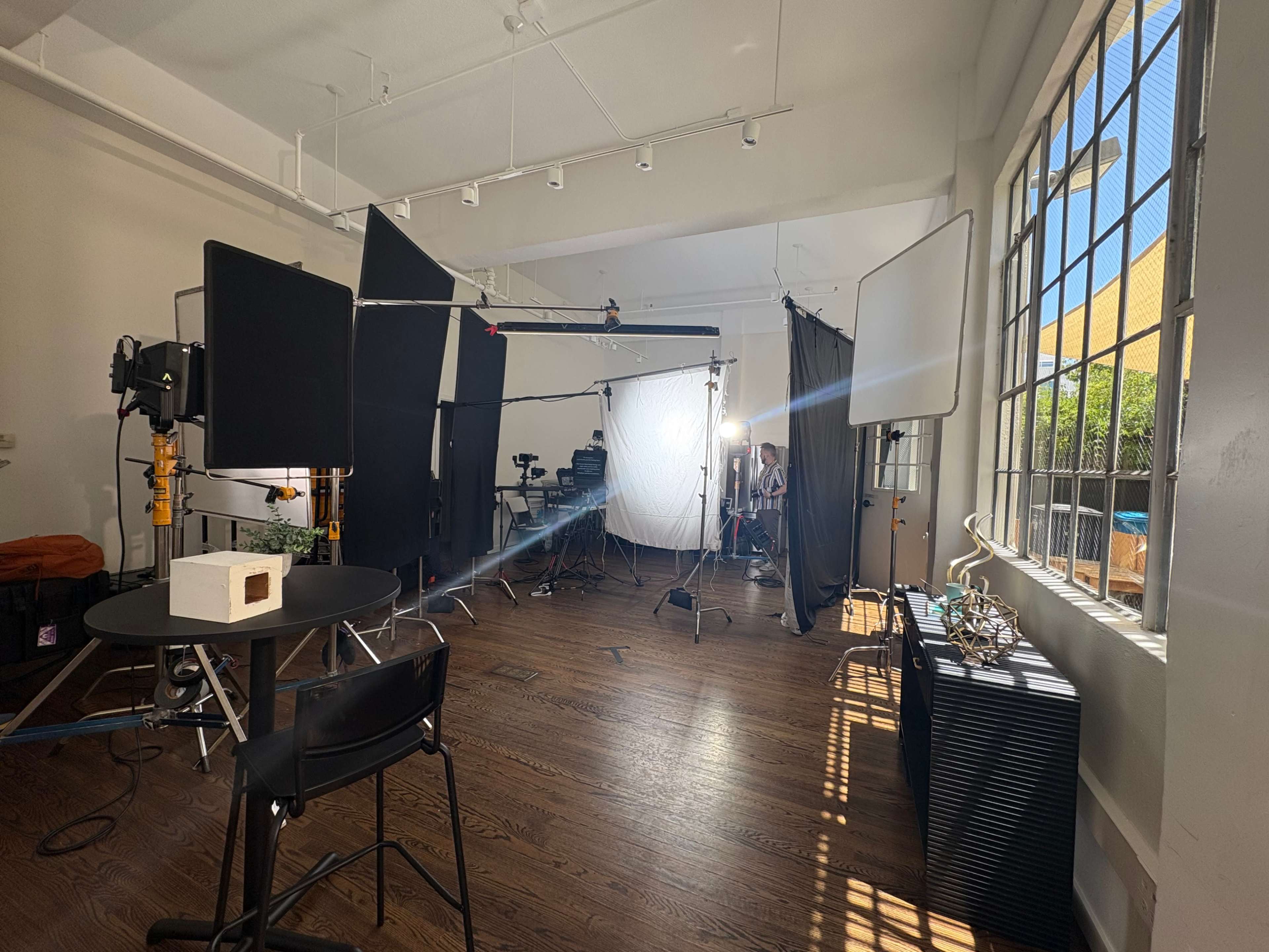 The image shows a well-lit studio setup with various photography equipment, including lights and backdrops, arranged around a central table.