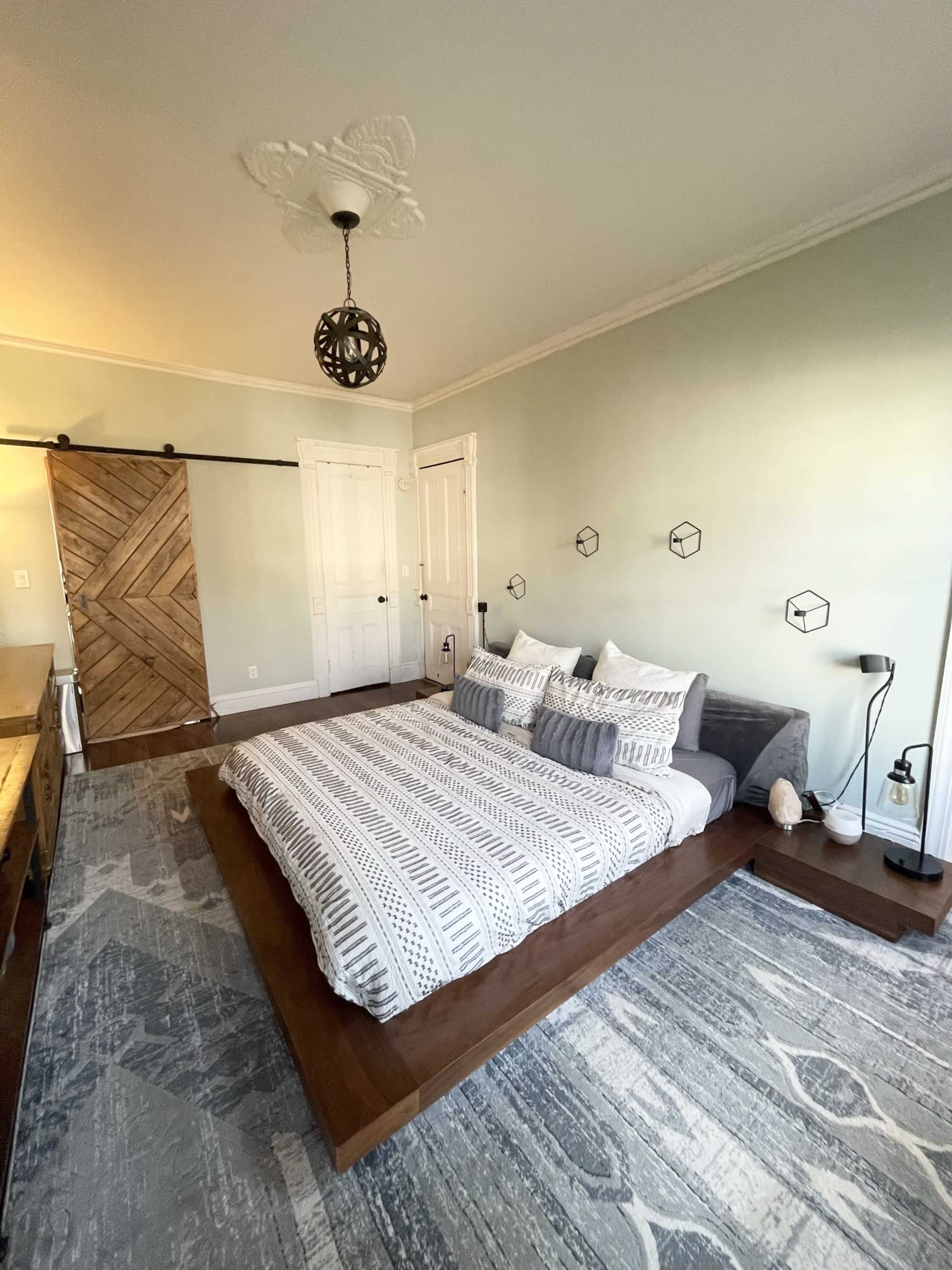 A minimalist bedroom with a low-profile bed on a wooden platform, against a light green wall, and featuring a sliding barn door.