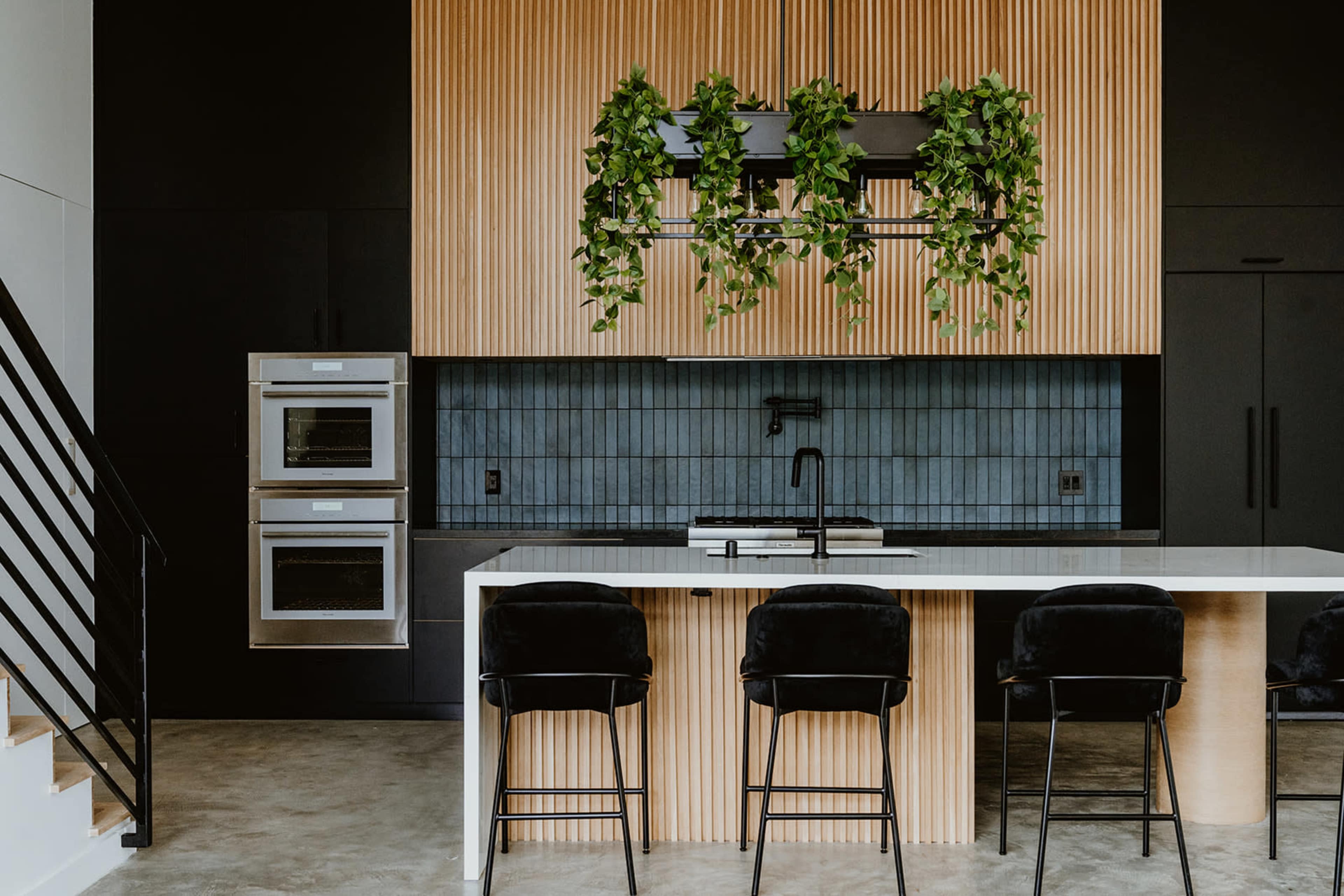 The image features a modern kitchen with wooden paneling, a black and blue tiled backsplash, and a central island with bar stools.