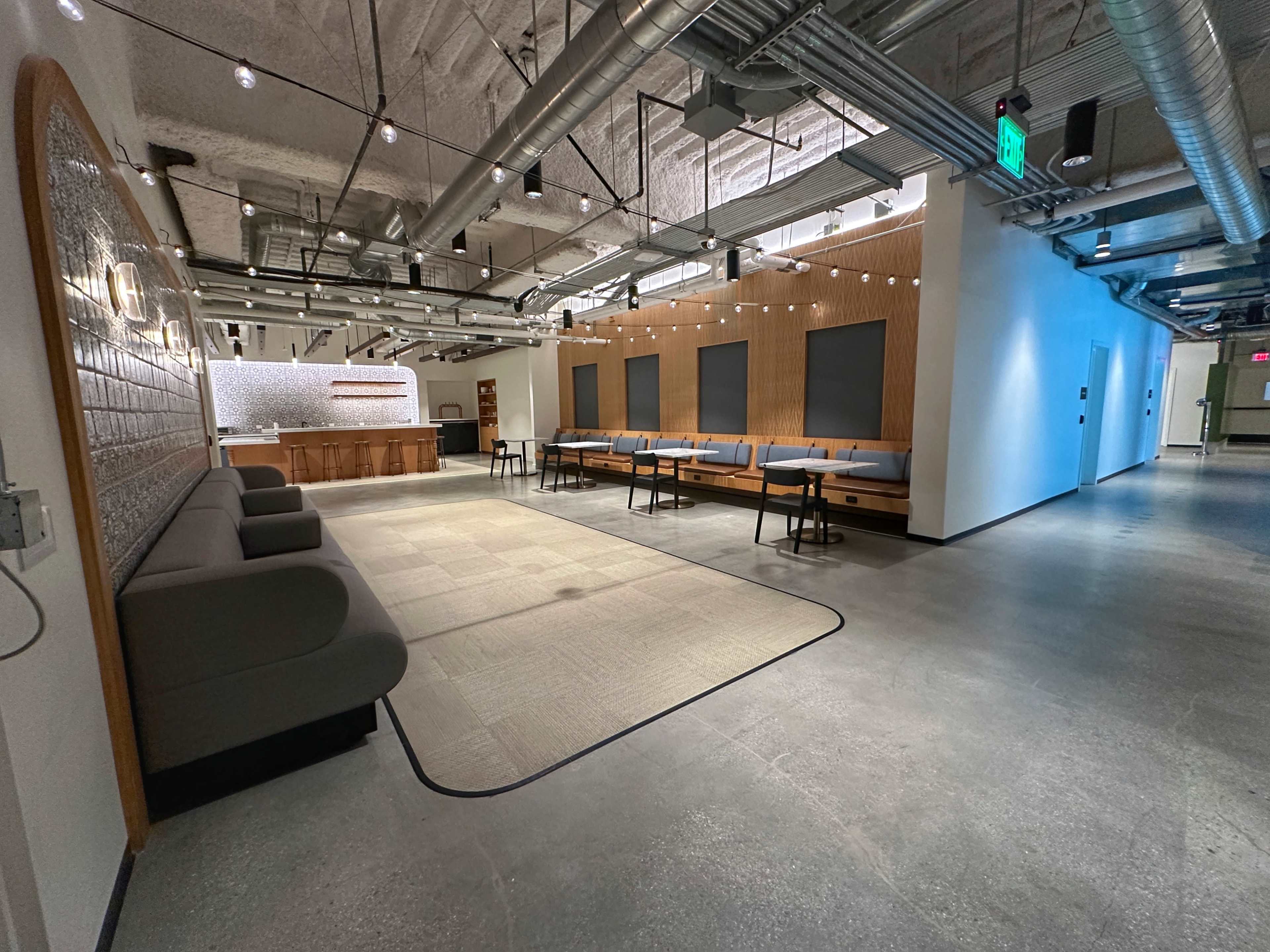 A spacious, modern hallway with a seating area on the left, a bar counter in the background, and rows of chairs arranged along the right side.