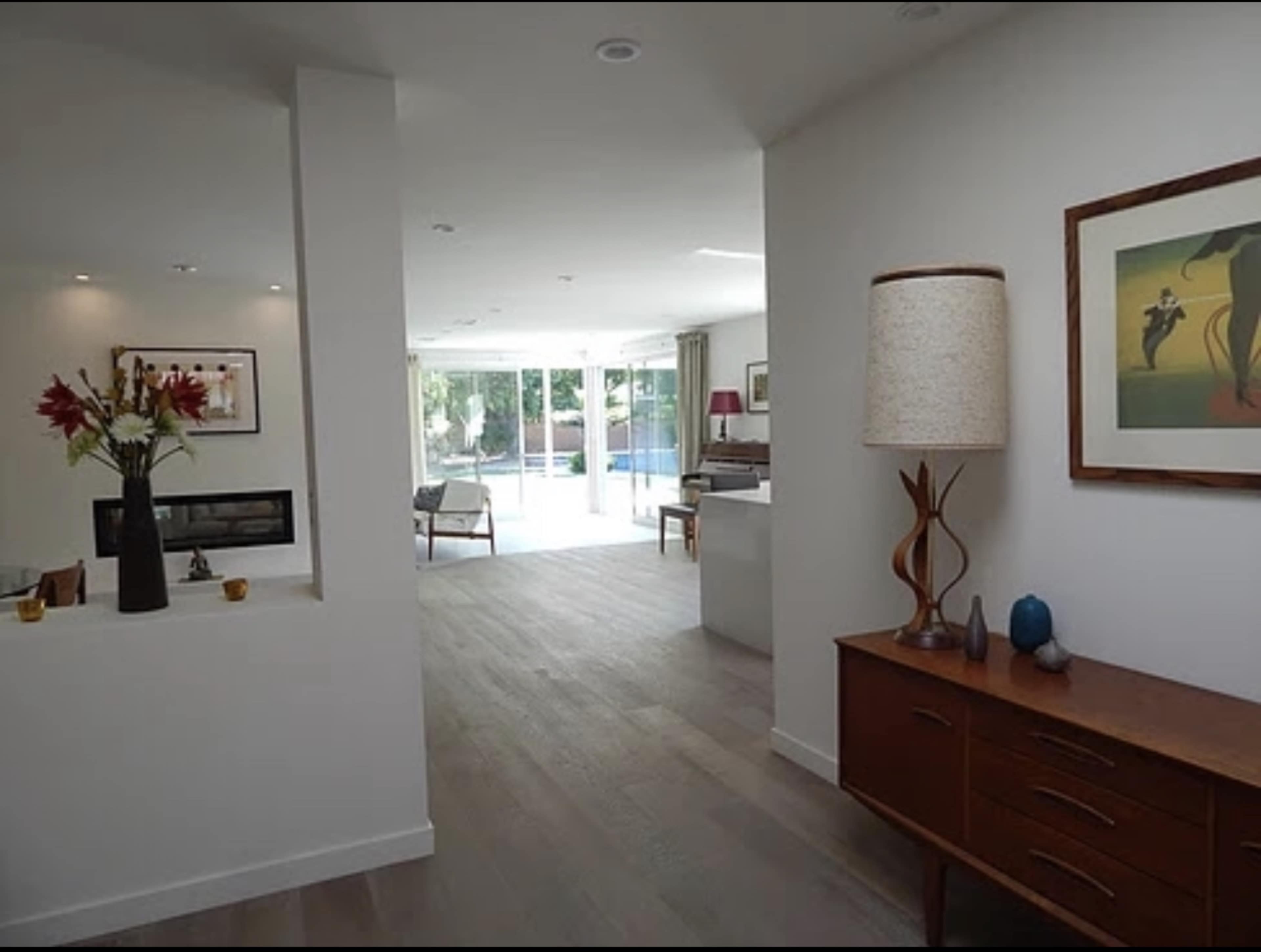 A modern entryway leads to a bright living area with large windows overlooking a pool.
