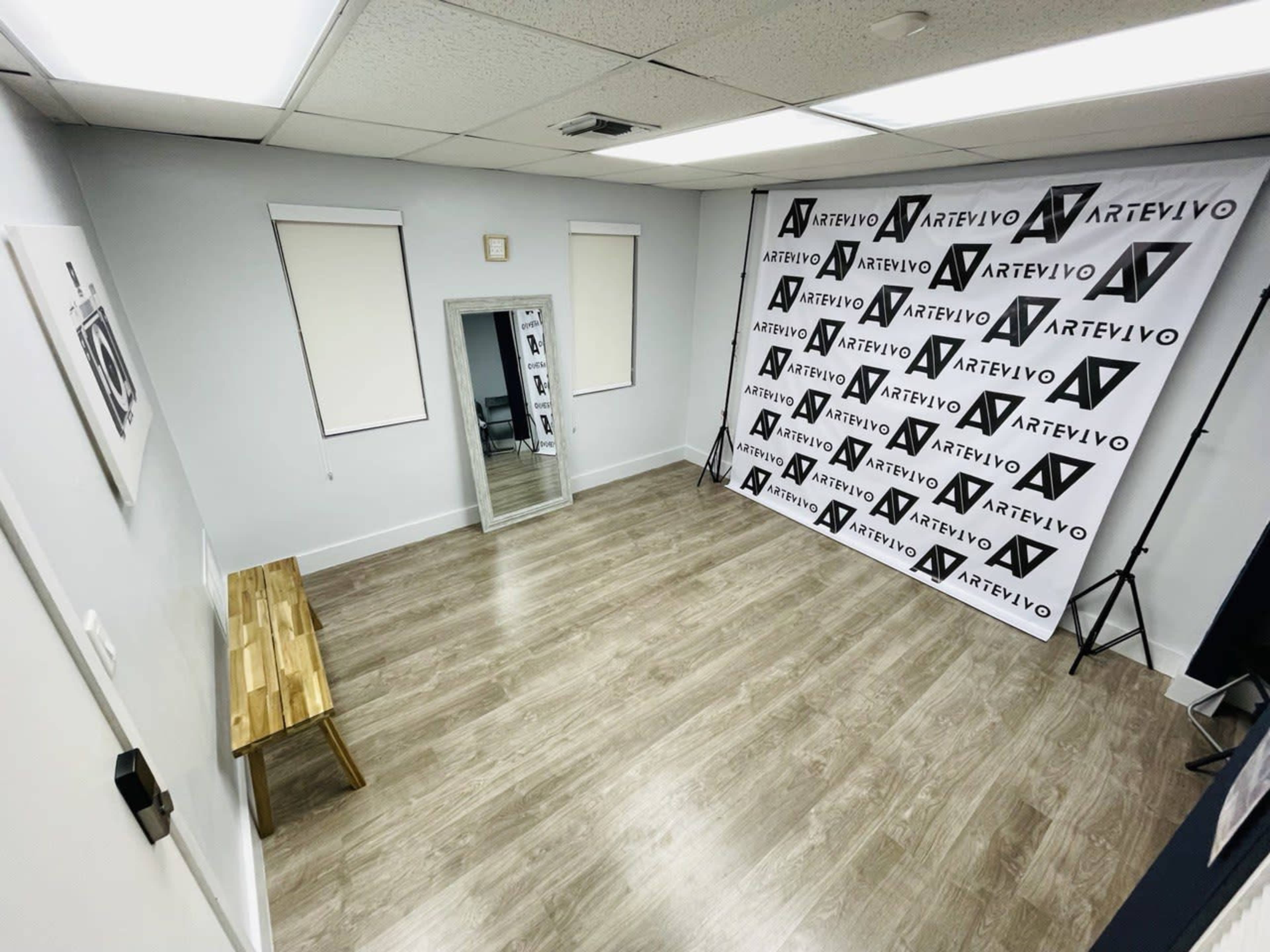 A sparsely furnished room featuring a wooden bench, a mirror, and a wall covered with repeated black and white logo designs.