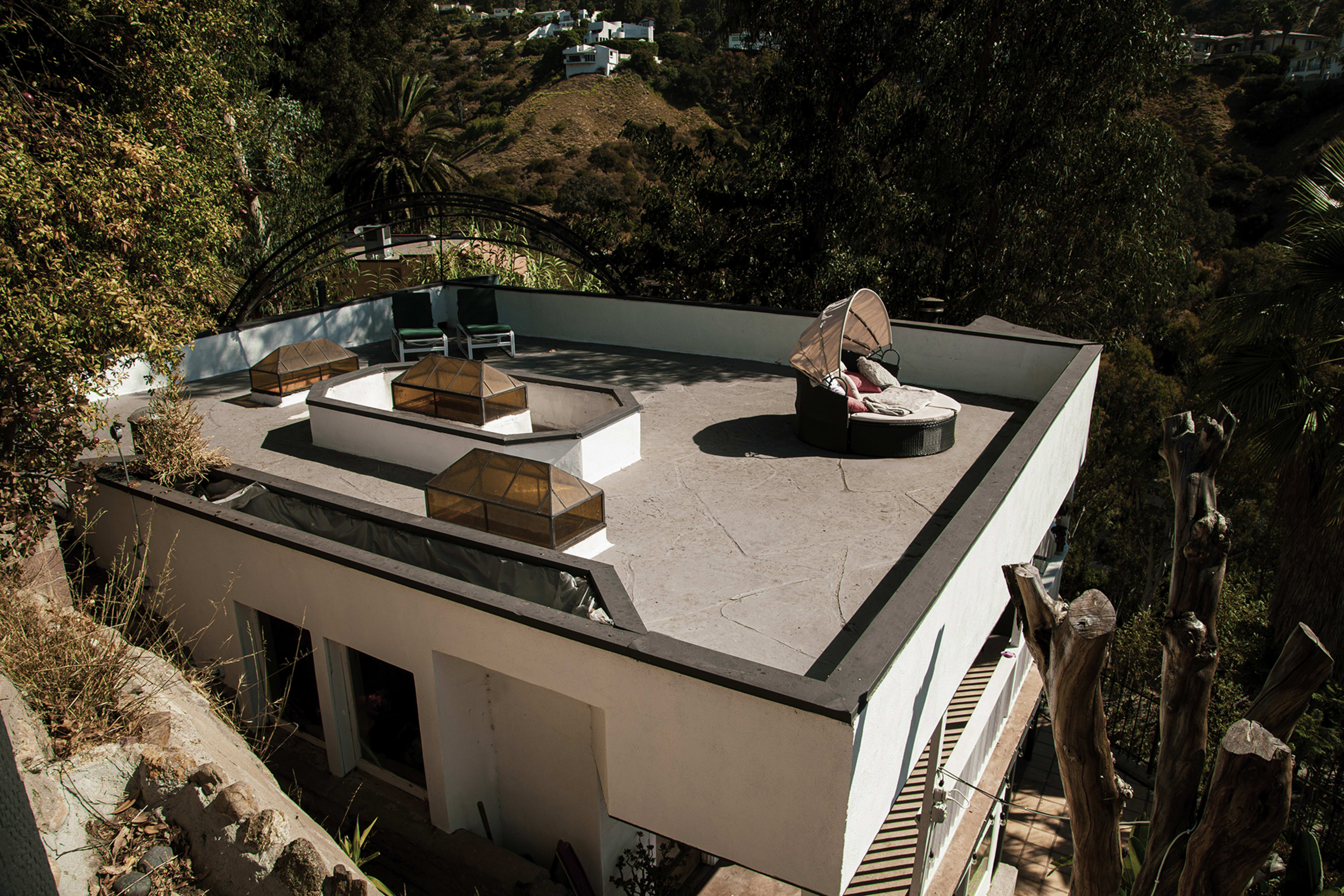 A modern rooftop terrace with lounge furniture and glass skylights surrounded by greenery and hills.