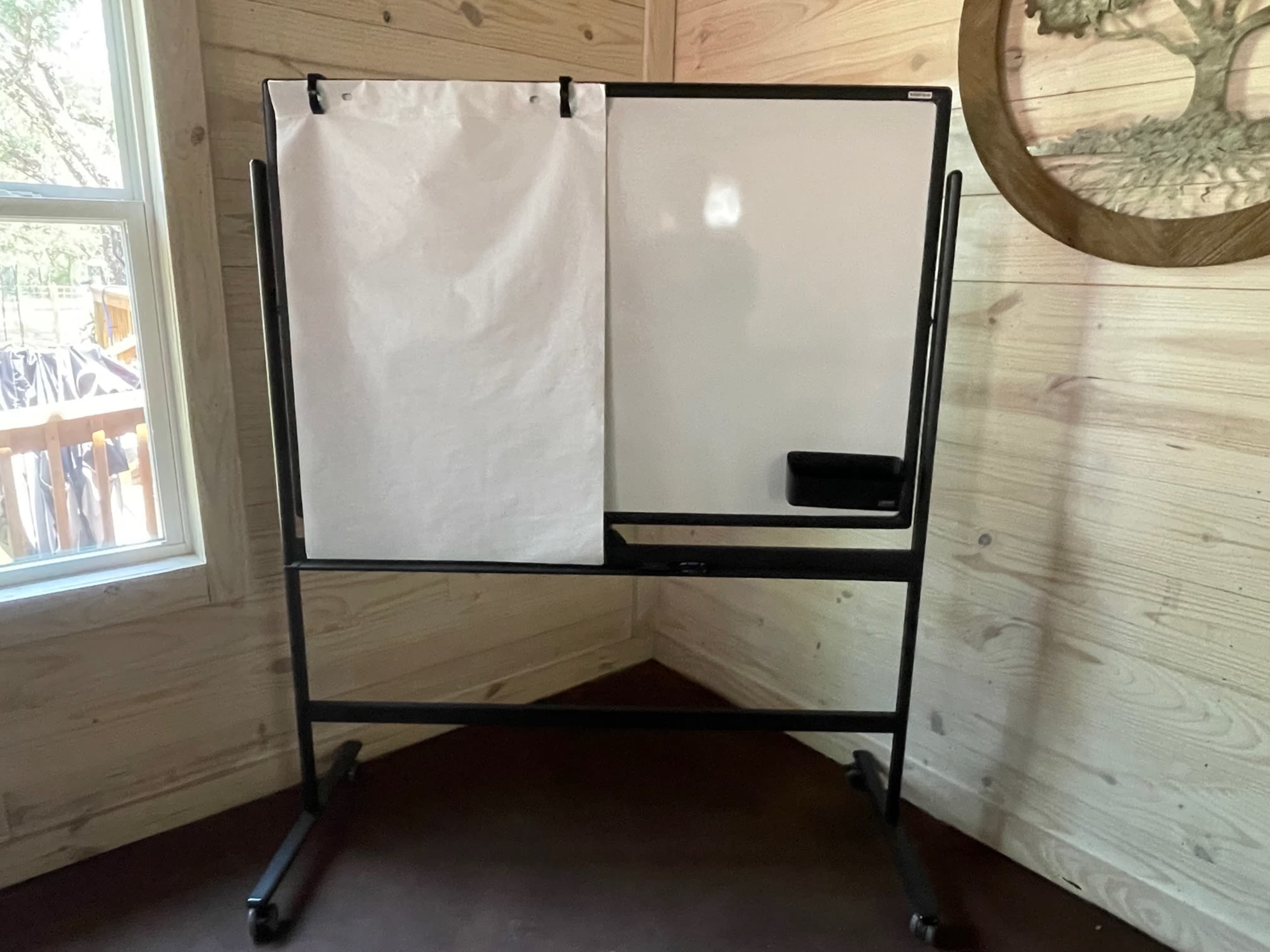 A mobile whiteboard with a removable paper pad sits in a corner of a wooden-paneled room.