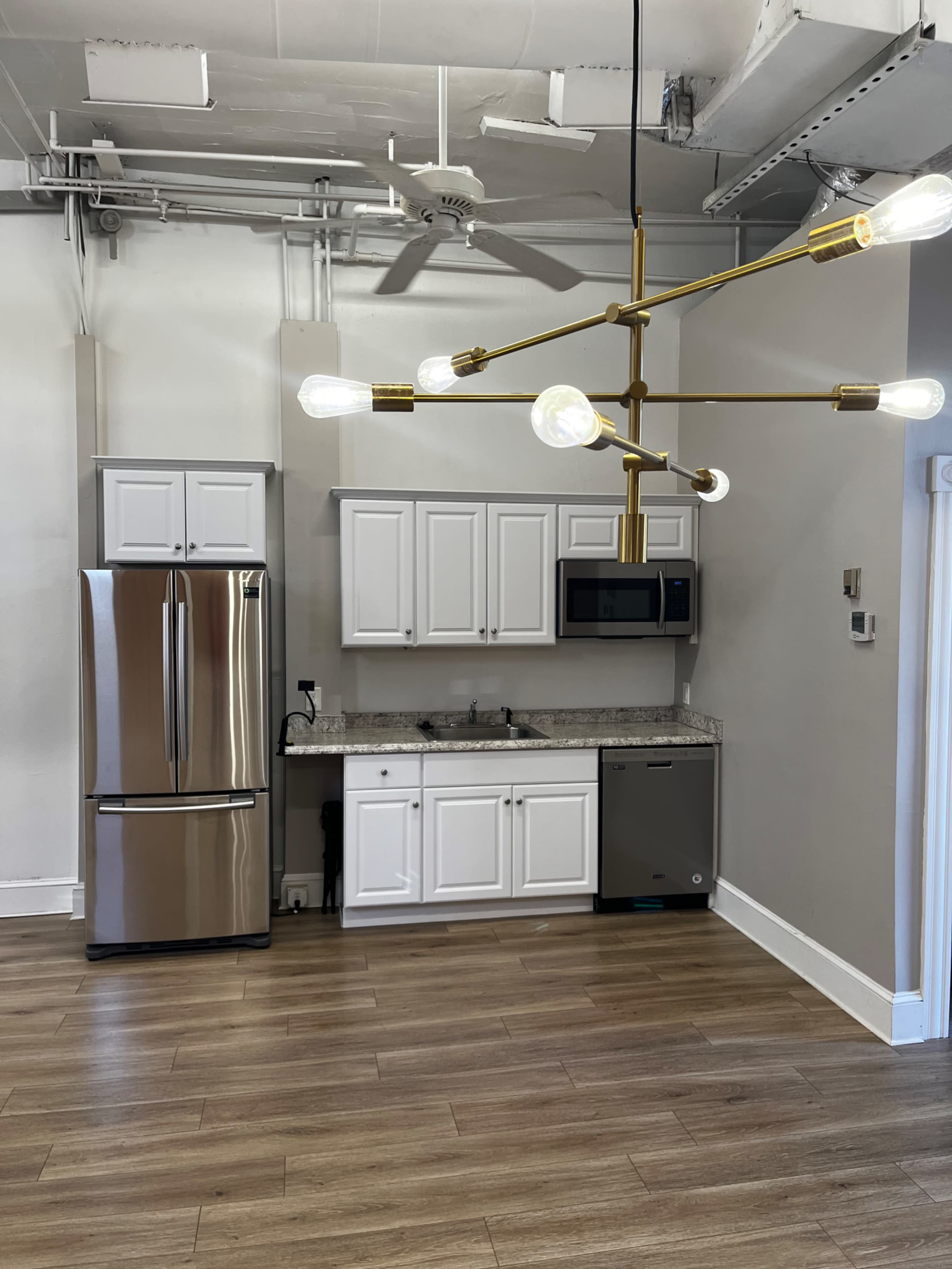 A modern kitchen featuring stainless steel appliances, white cabinetry, and a chandelier with multiple light bulbs.