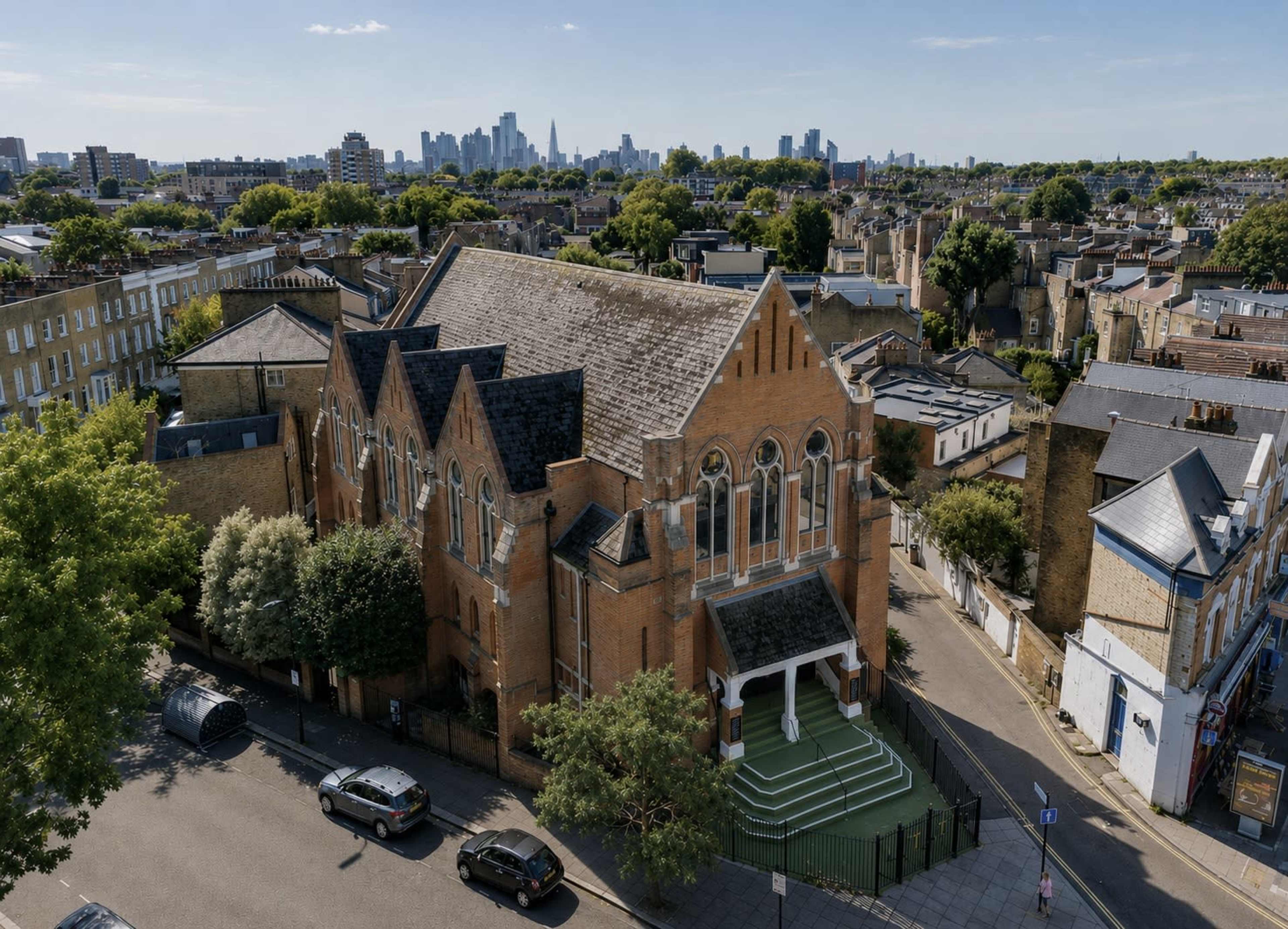The image shows a large brick building with pointed arches and a tall spire, surrounded by residential streets and a skyline of skyscrapers in the background.