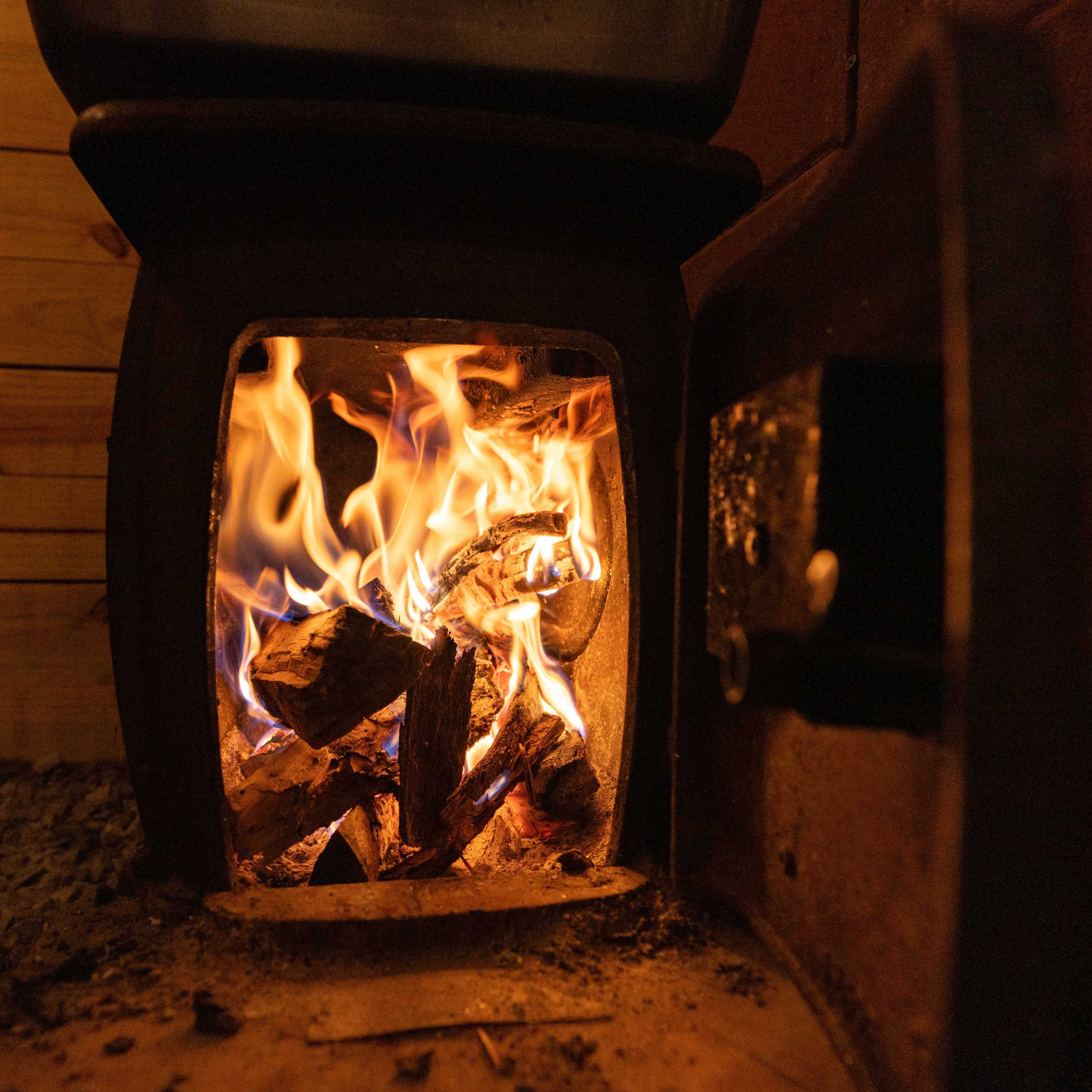 A wood stove with flames and burning logs visible through the open door.