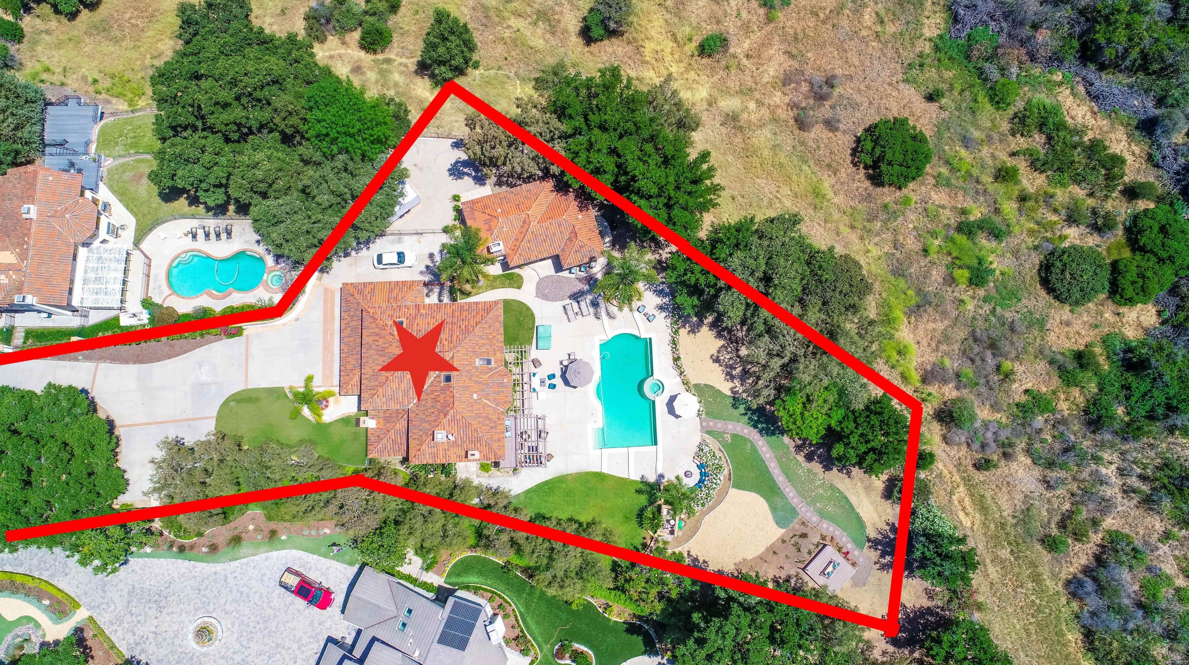 An aerial view of a spacious property featuring a house, a swimming pool, and landscaped areas, outlined in red with a star marking the central building.