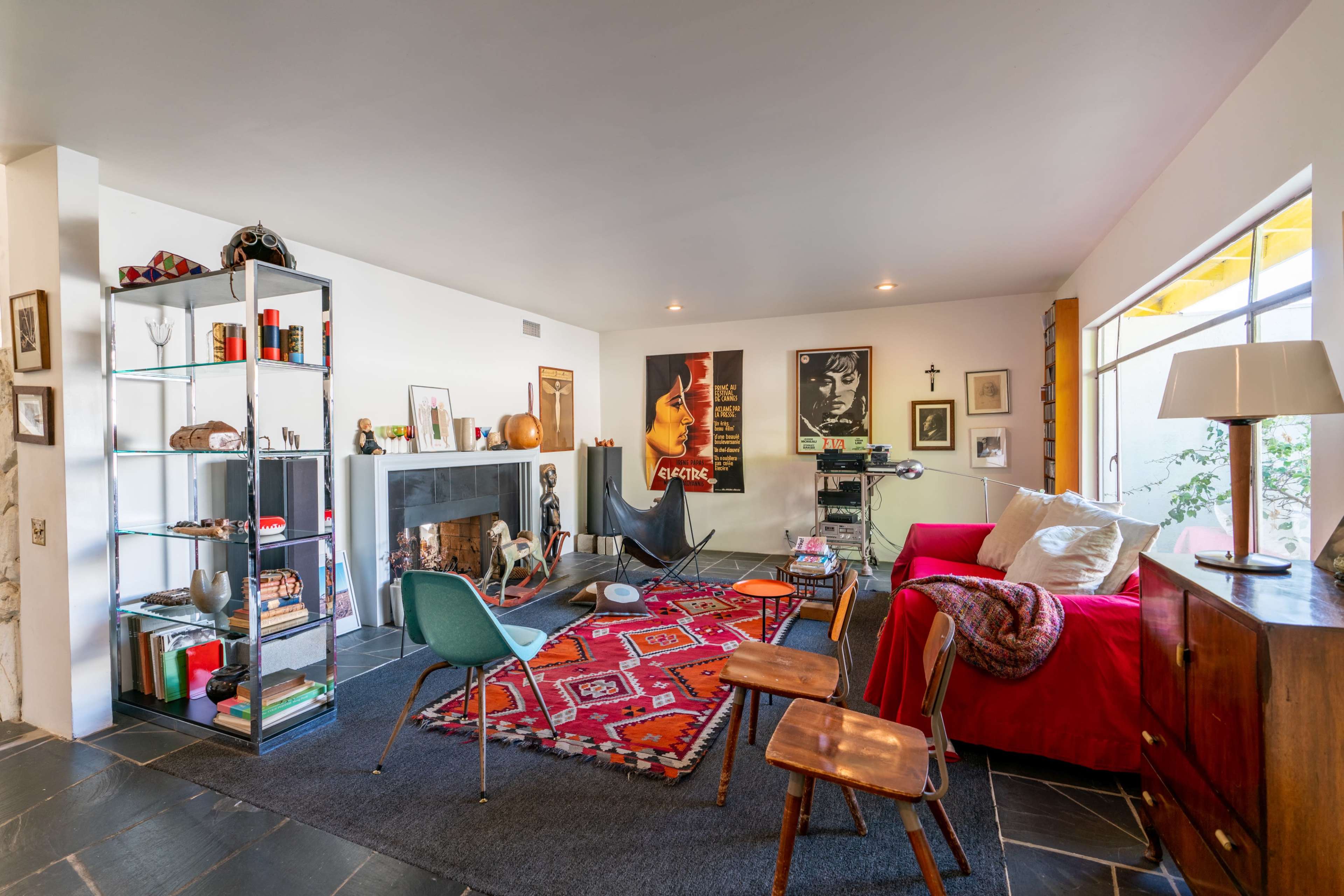A modern living room with a red sofa, a patterned rug, a bookshelf, and various decorative items, including a fireplace and art on the walls.