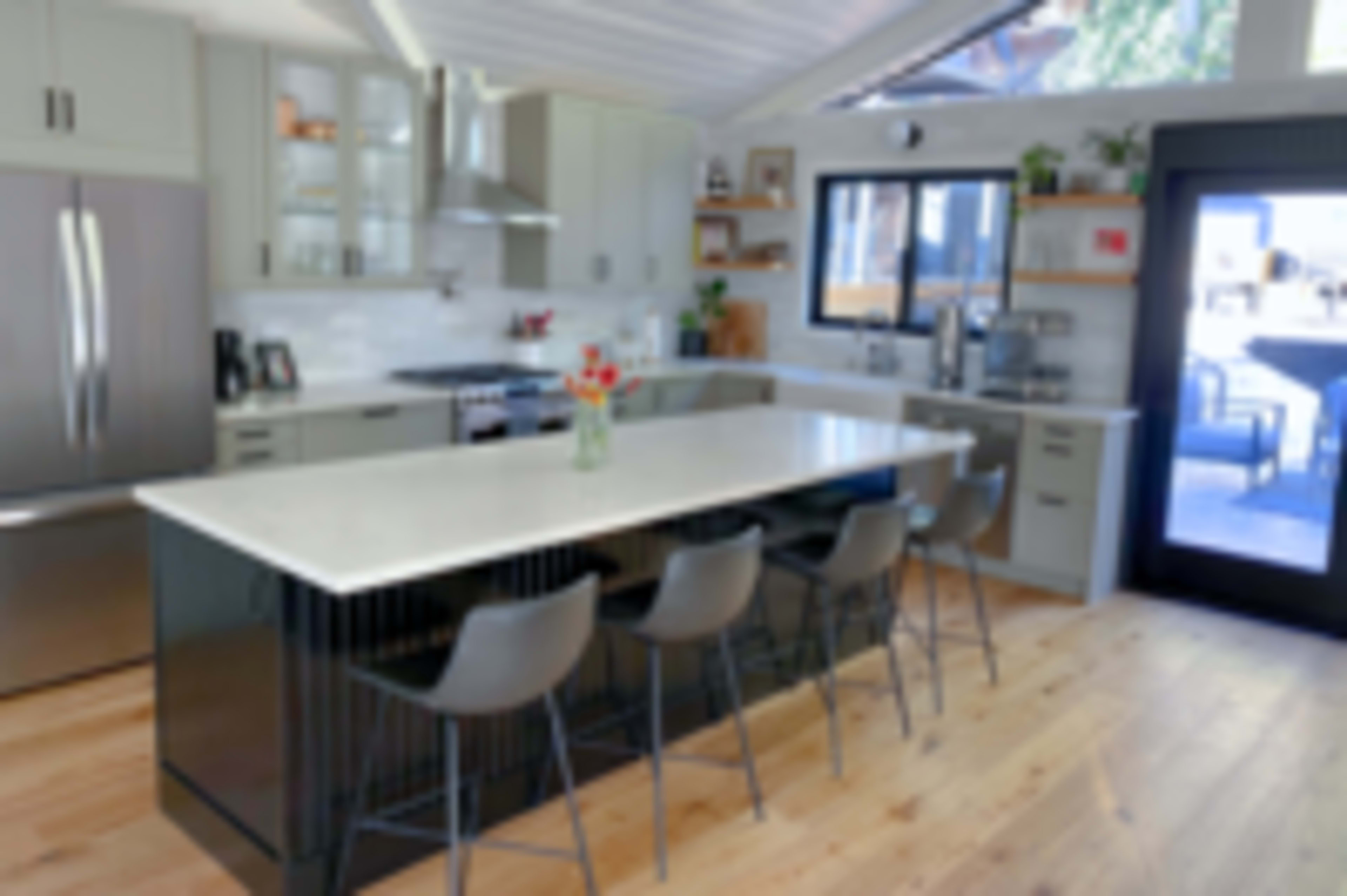 The image shows a modern kitchen featuring a central island with seating, stainless steel appliances, and light wood flooring.