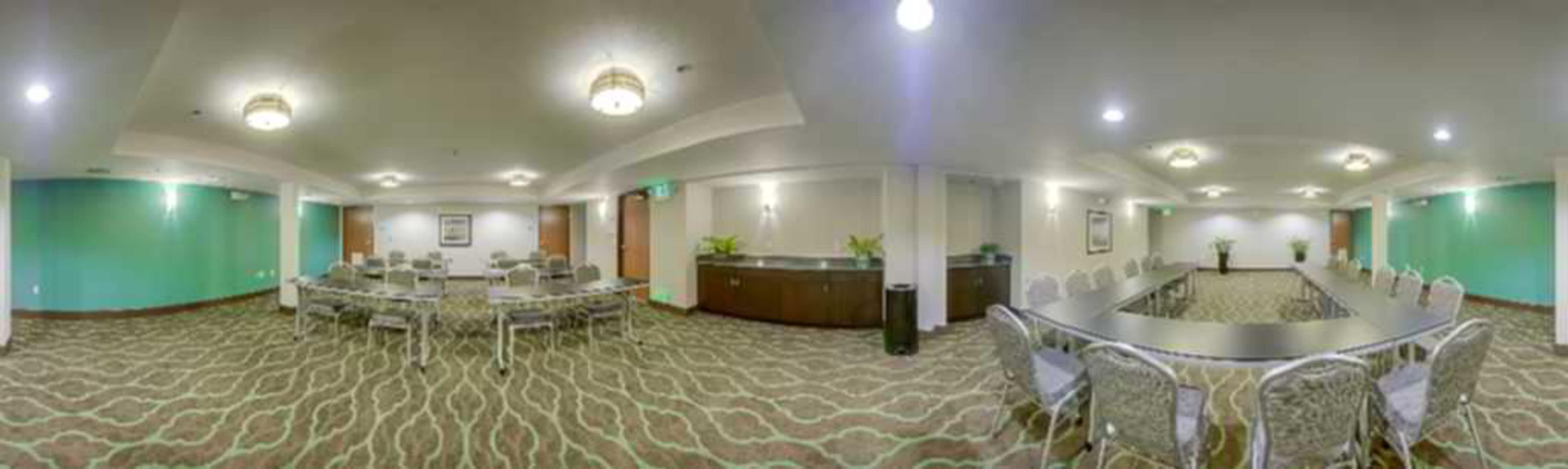 The image shows a spacious conference room with seating arrangements including a long table and multiple round tables, complemented by green accent walls and decorative lighting.