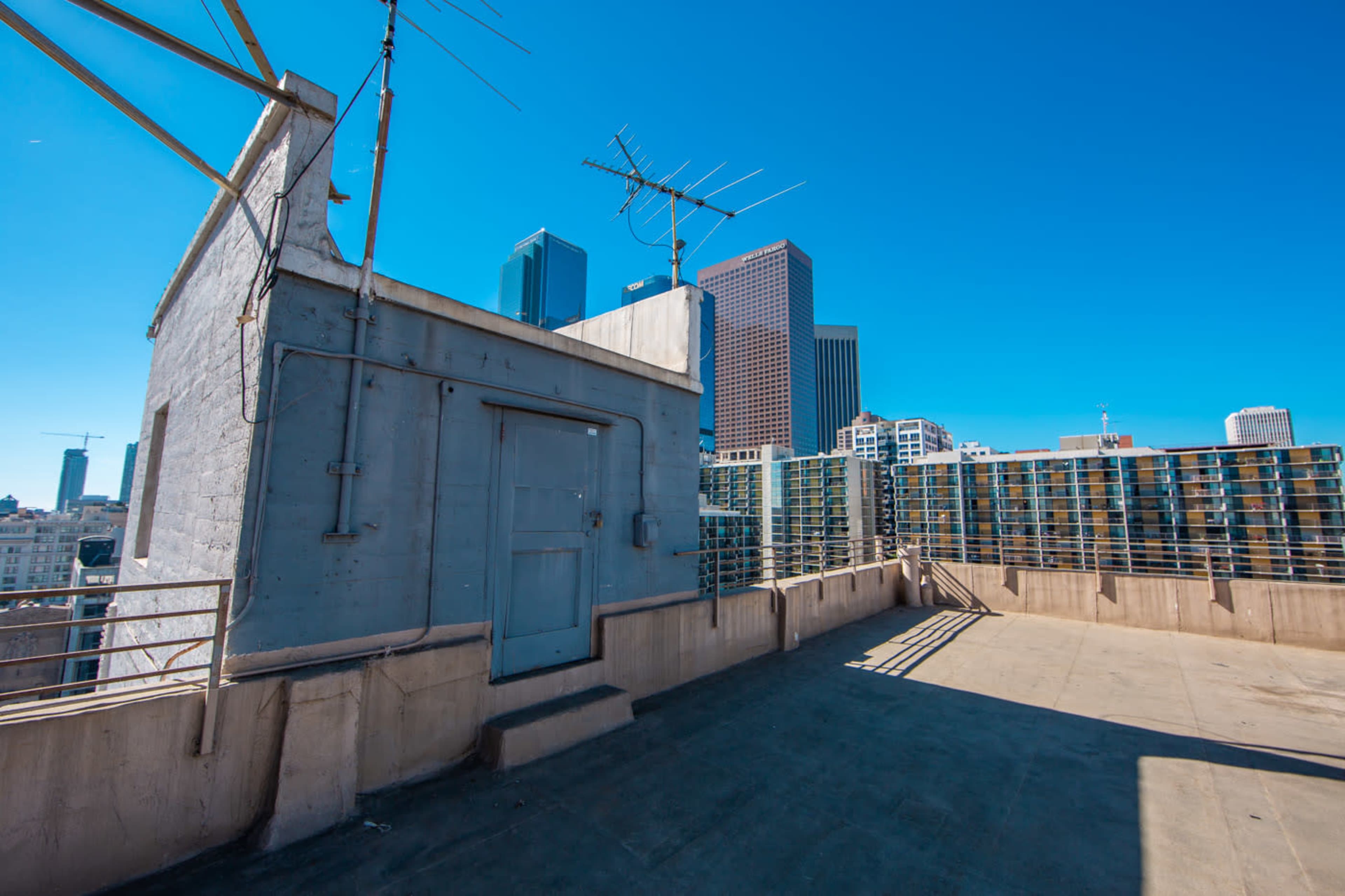 The image shows a rooftop area with a concrete structure and several buildings in the background, under a clear blue sky.