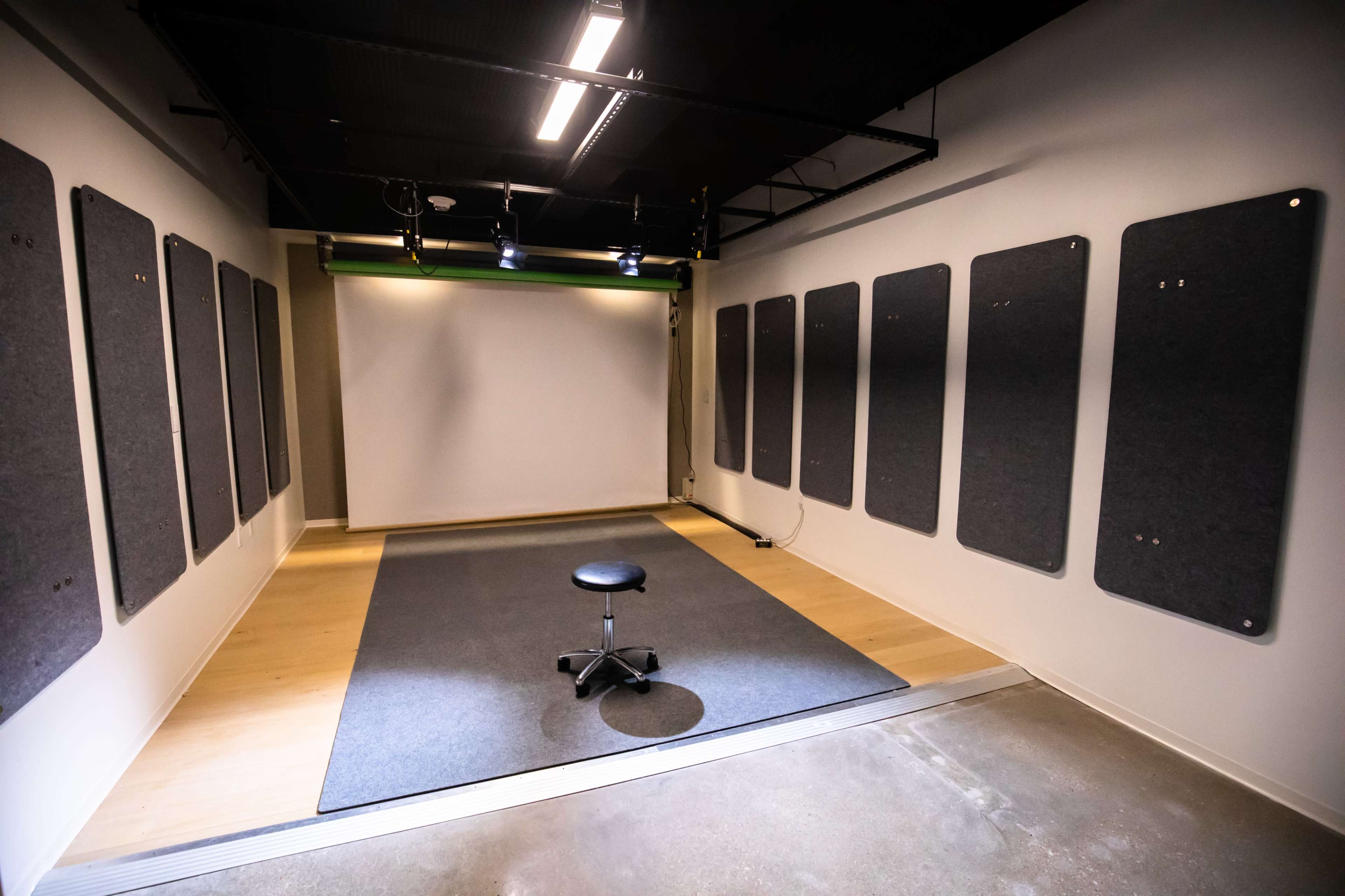 An empty room with a central stool on a gray mat, surrounded by several sound-absorbing panels mounted on the walls.