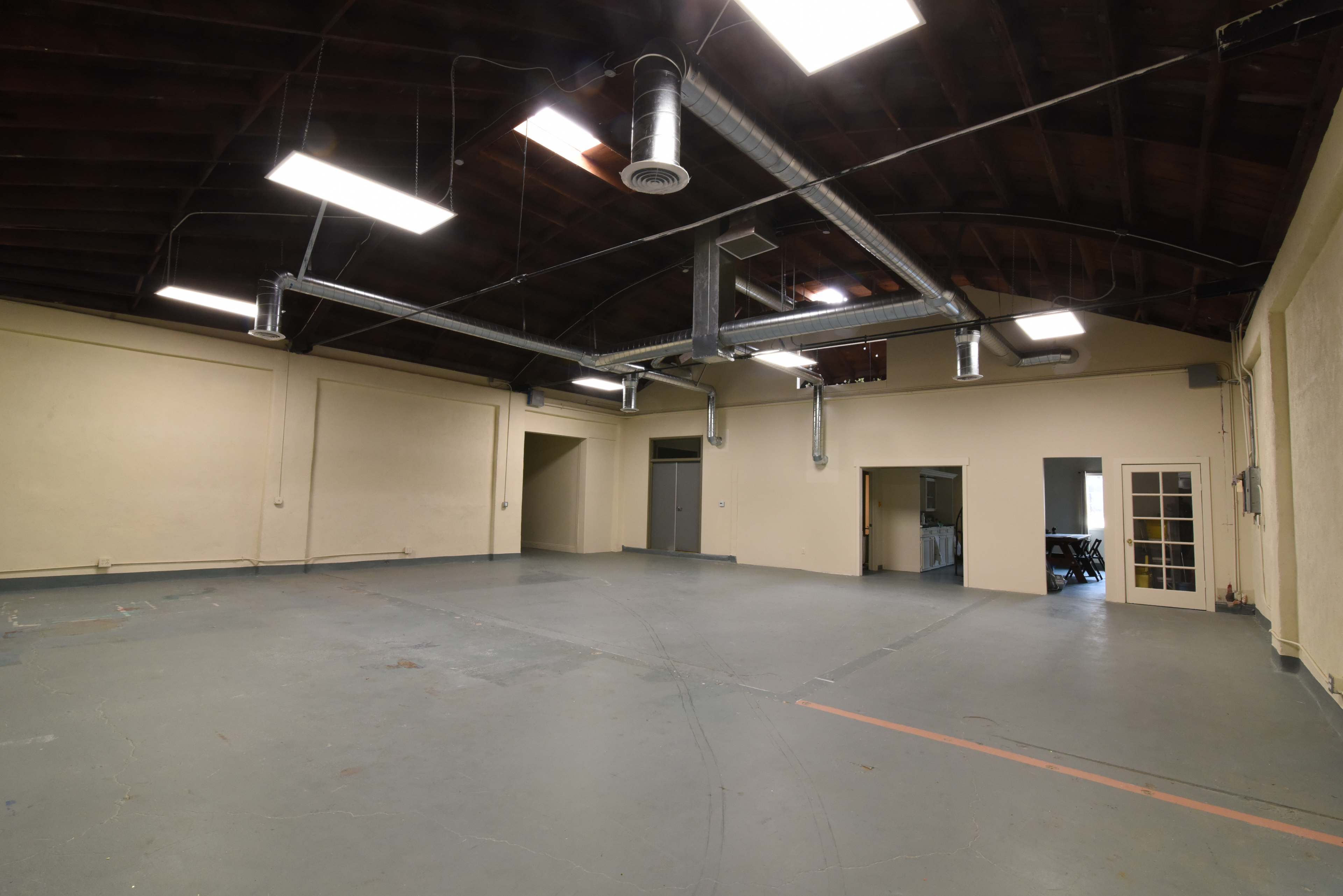 A large, empty industrial space with high ceilings, multiple overhead lights, and visible ventilation ducts.