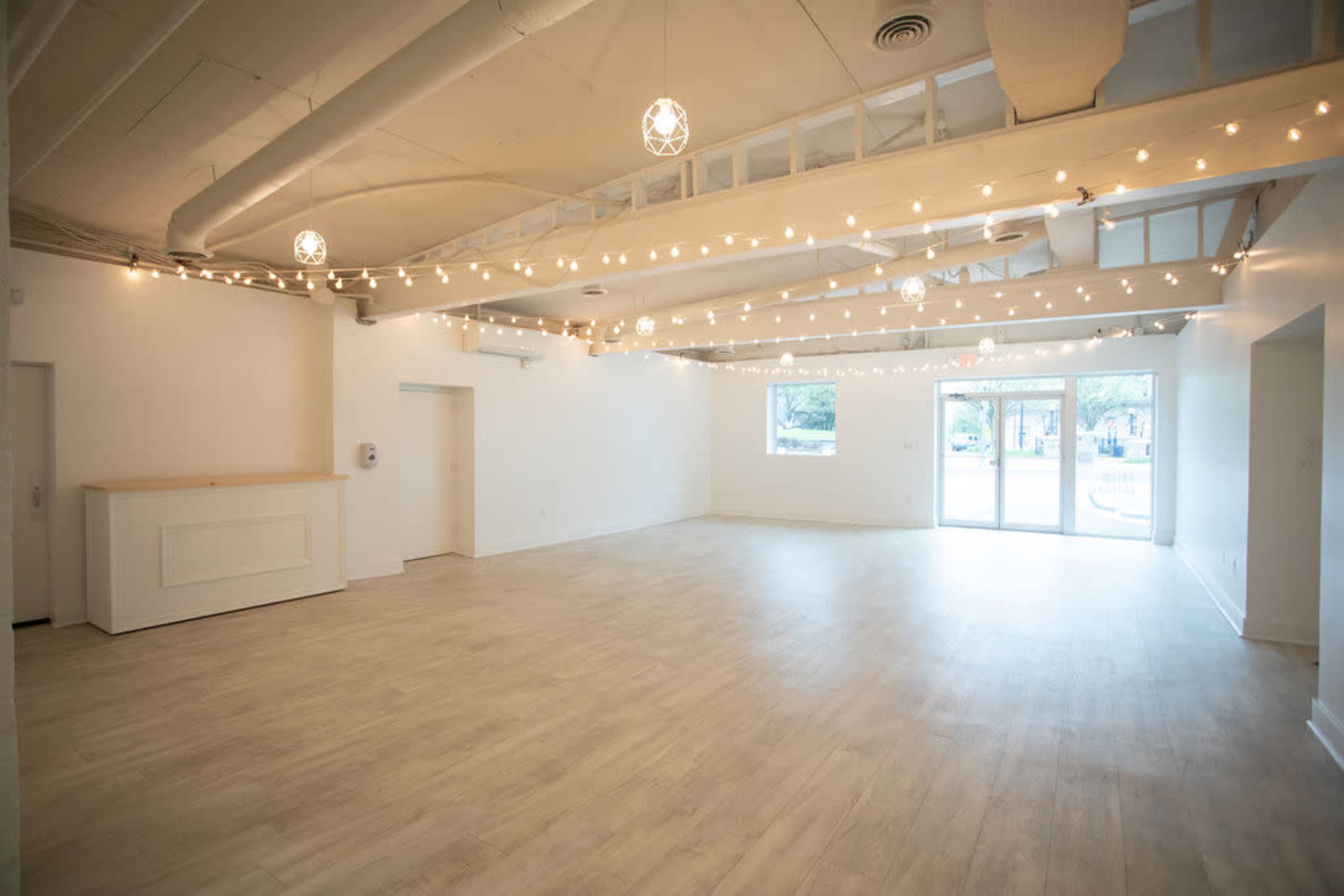 A spacious, empty room with light wooden flooring and string lights hanging from the ceiling.