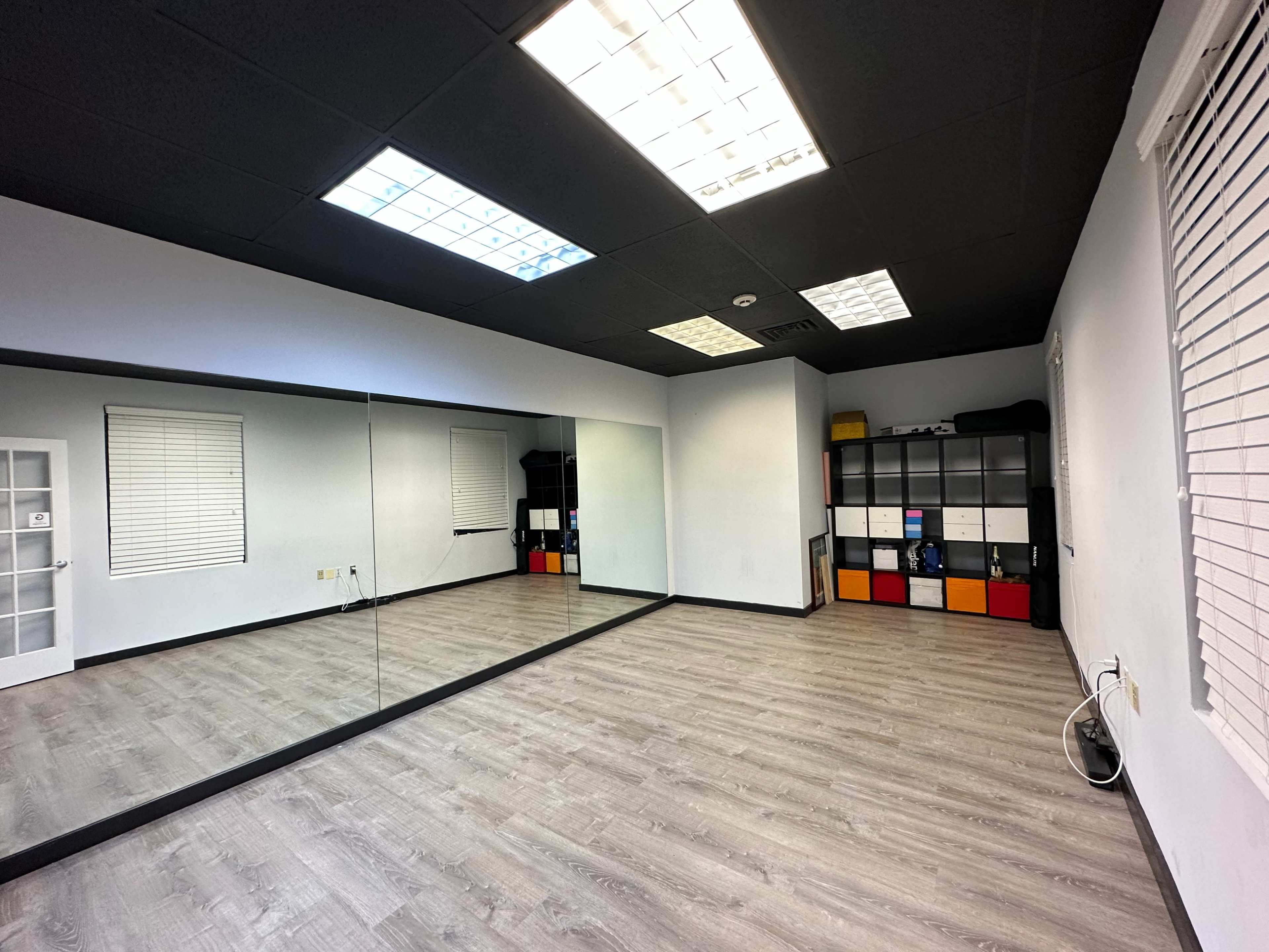 An empty room with a large mirror on one wall, gray flooring, and a set of black and white storage units against the opposite wall.