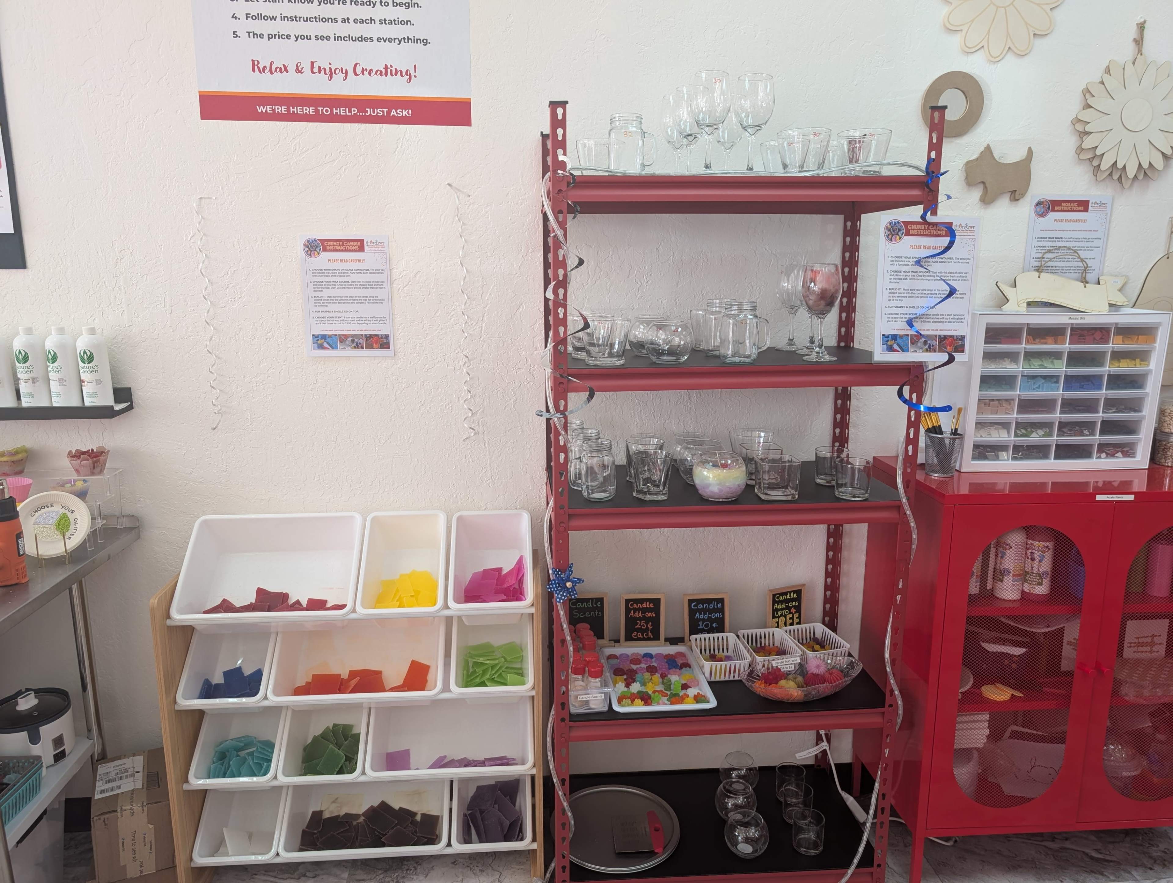 The image shows a shelf with transparent glassware and colorful pieces of paper or plastic arranged in trays, alongside a display of craft supplies and instructional materials.